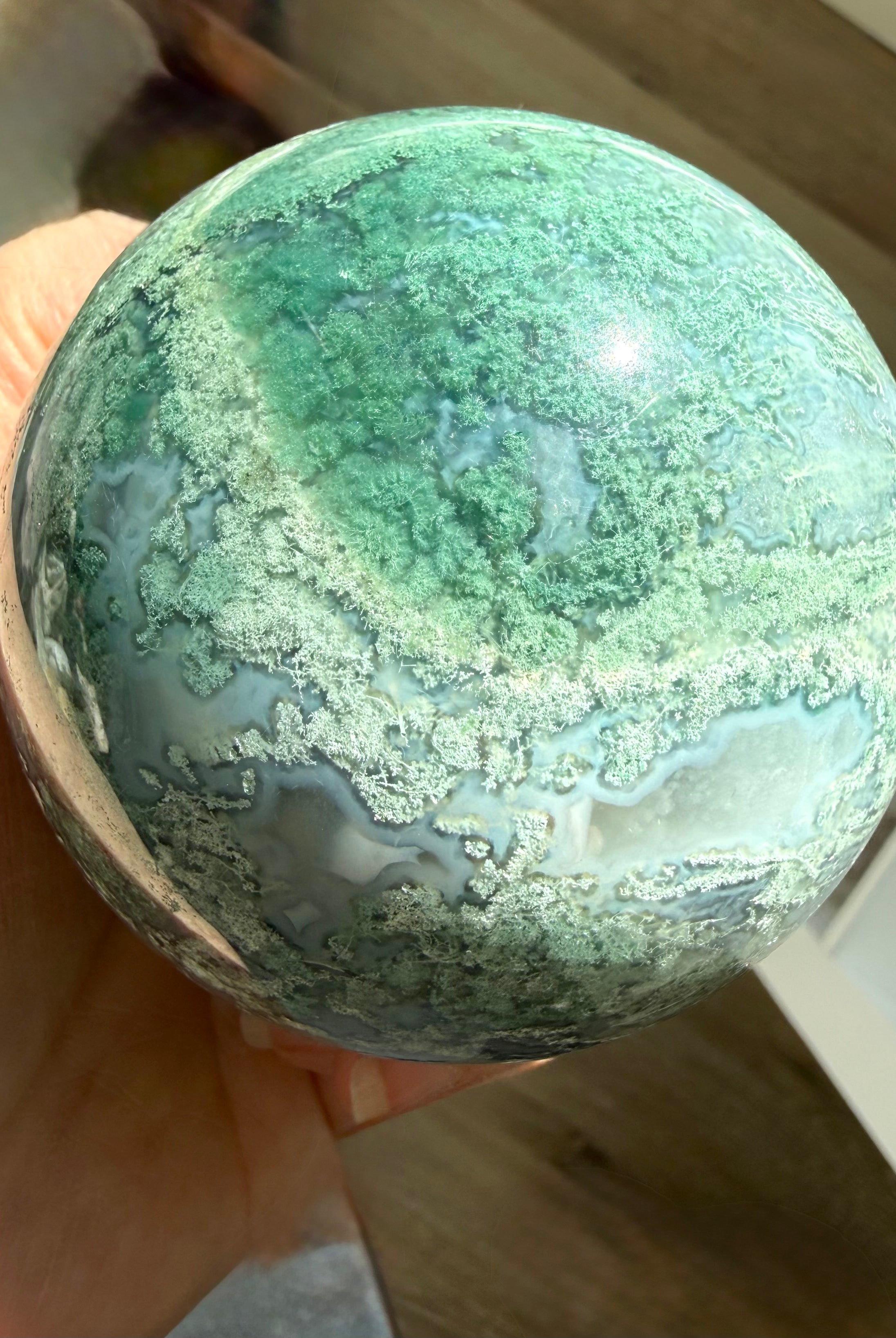 Lacy Moss Agate sphere in bright sunlight showing vivid green patterns, Quartz veins, and natural crystal details