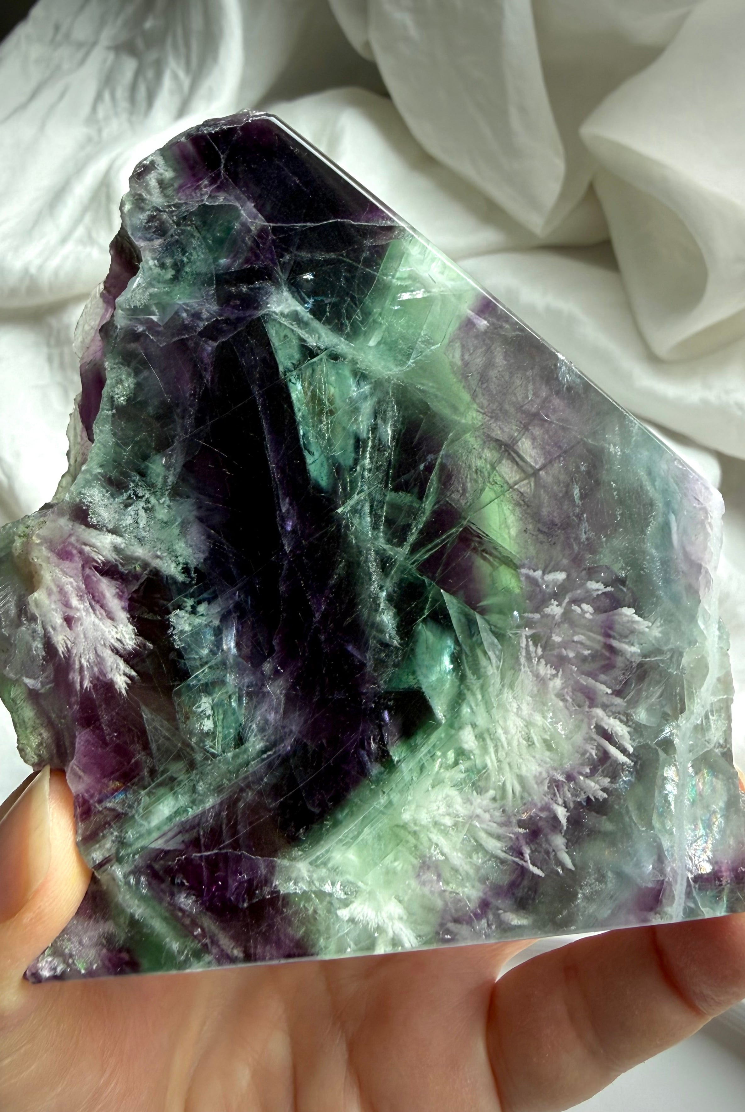 Polished fluorite slab photographed in natural light highlighting layered green and violet color zoning with rainbows