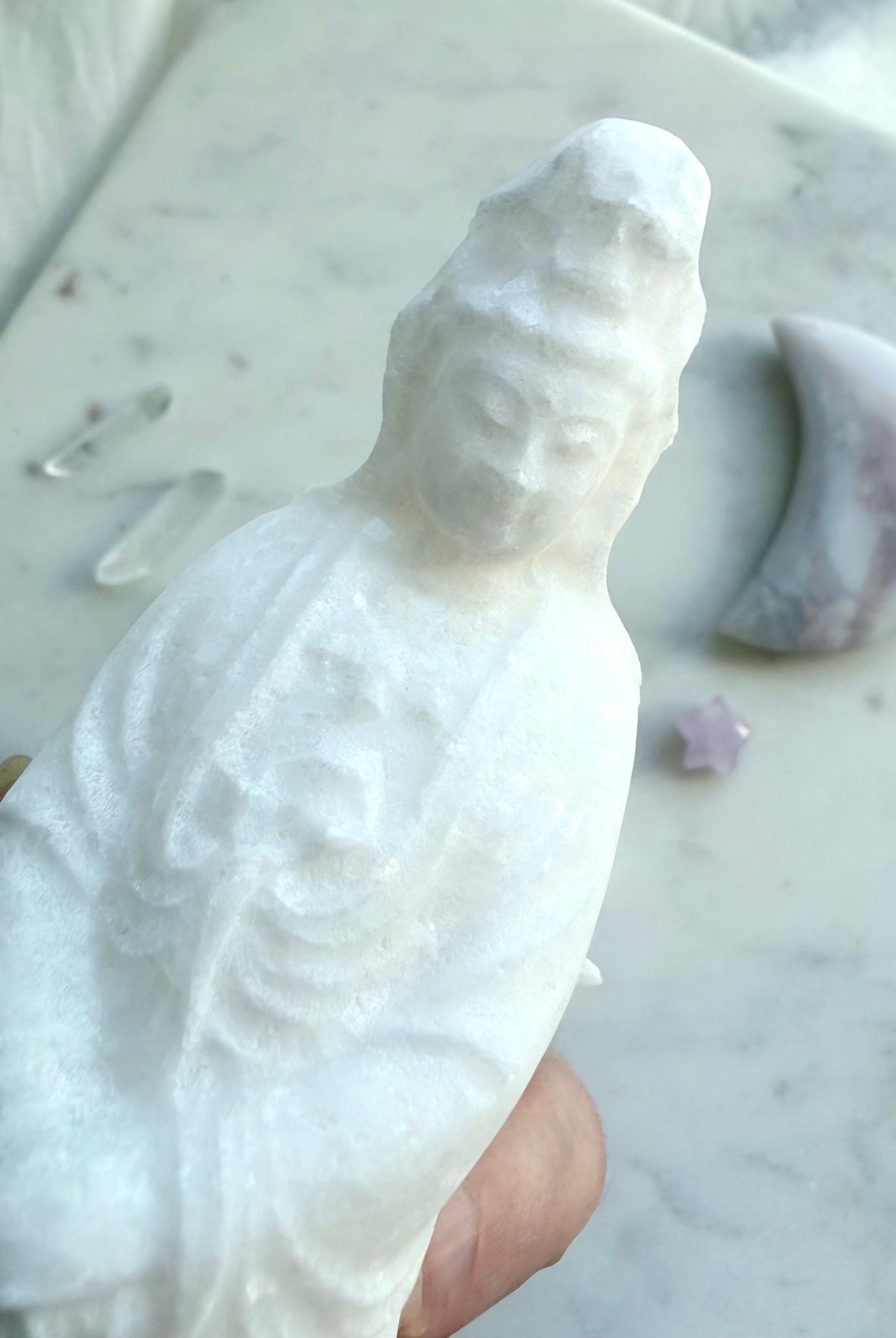 Close up White Jade Quan Yin carving held in hand beside crystal decor for scale and detail