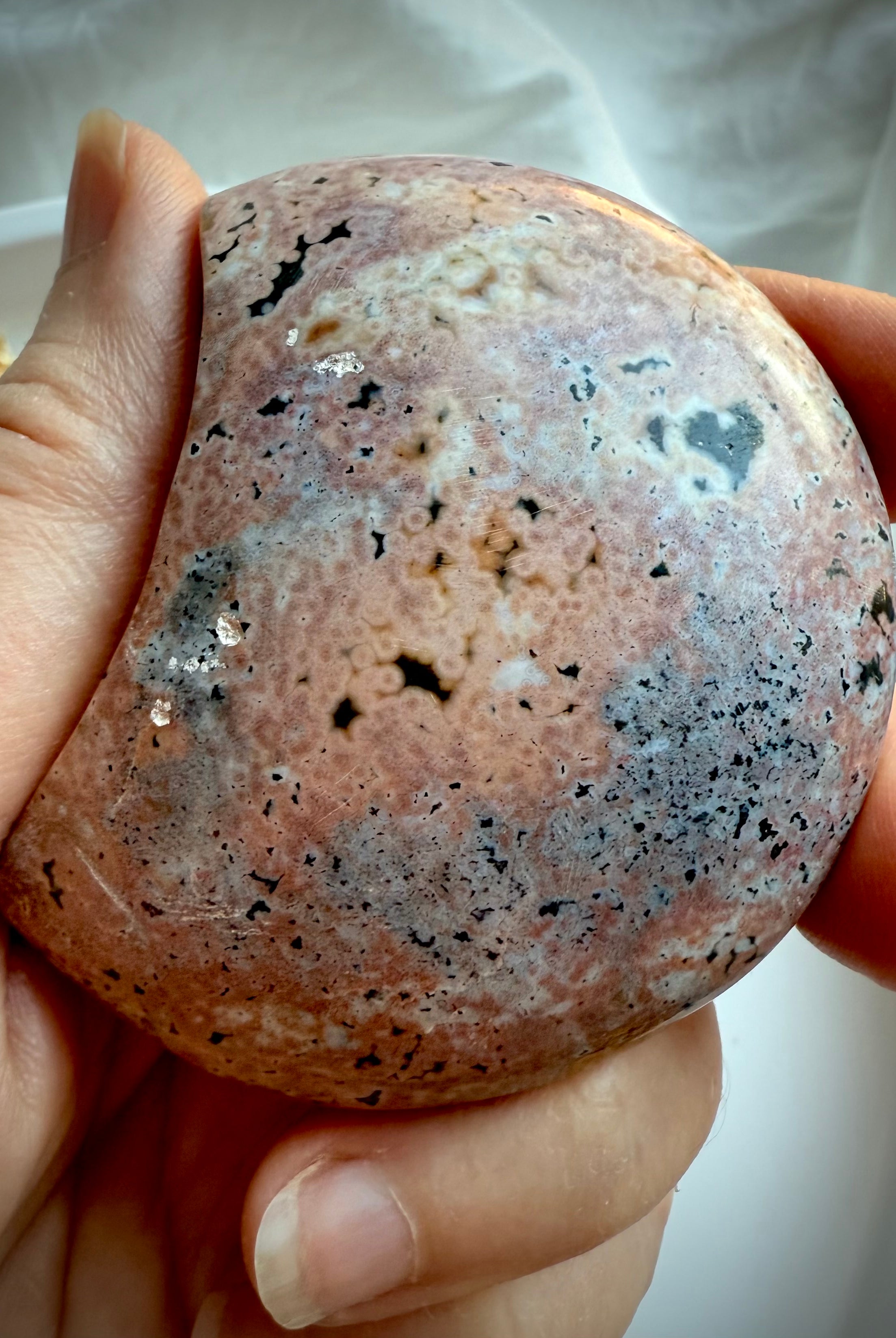 Polished Ocean Jasper moon in warm pink and tan tones with starburst orbicular markings held in hand