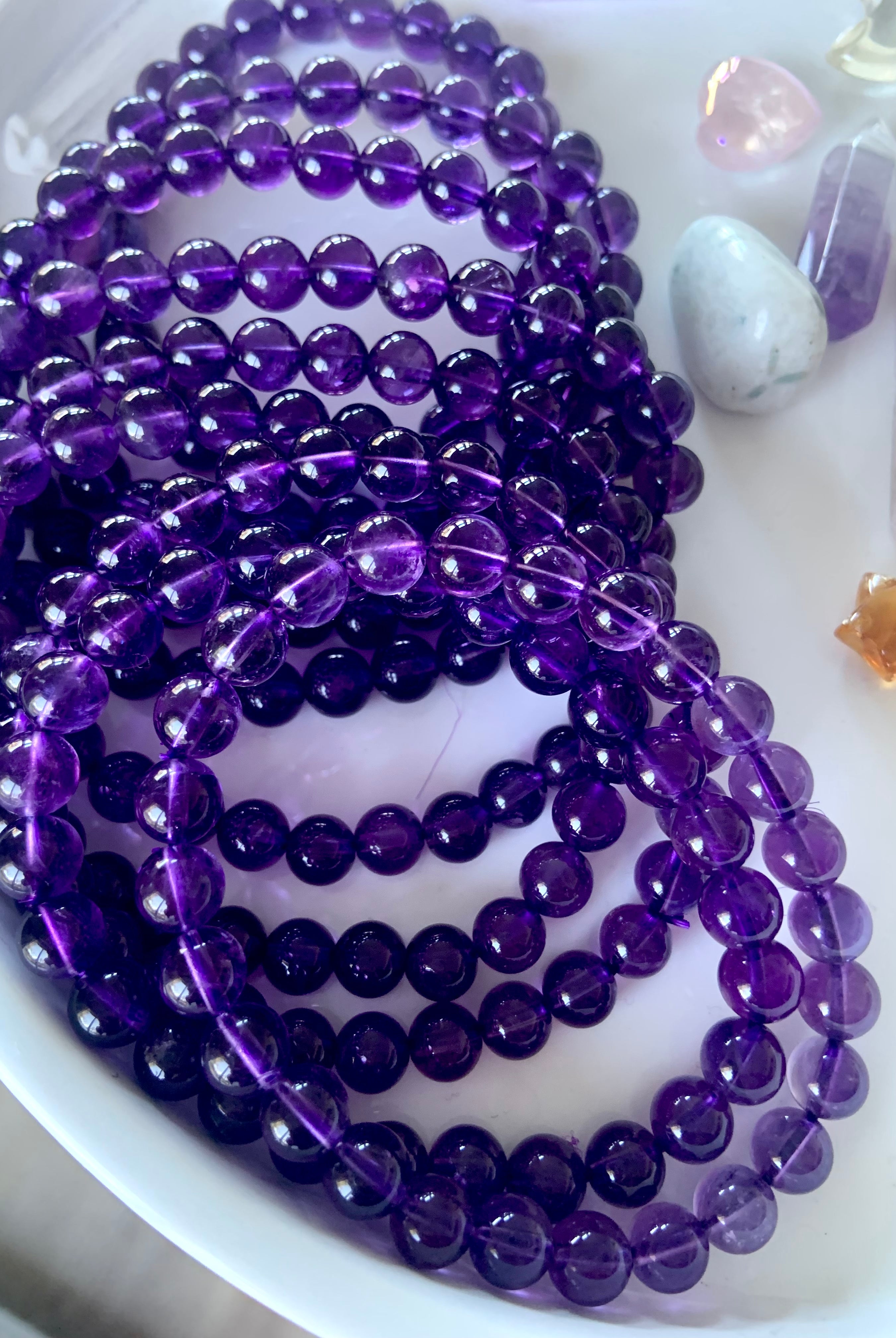 An array of high quality deep purple amethyst beaded bracelets on a white plate with other mini crystals in the background