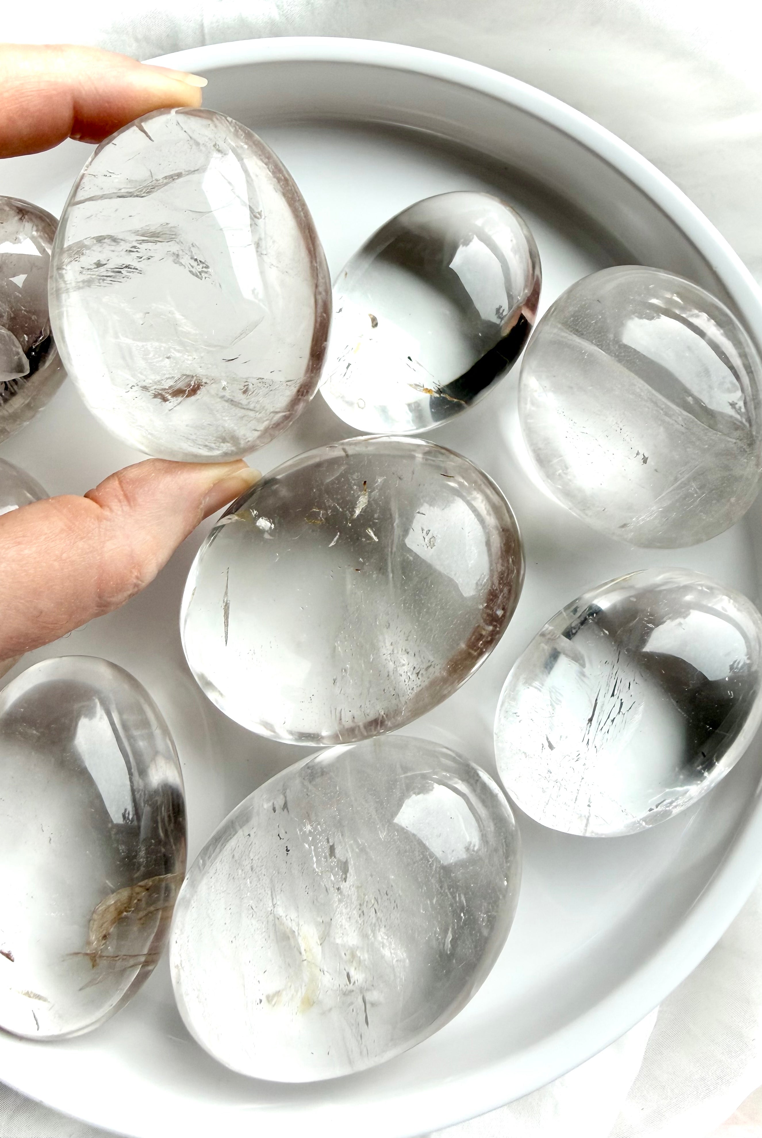 clear quartz palm stones on white tray with one held to the light showing high clarity and natural inclusions