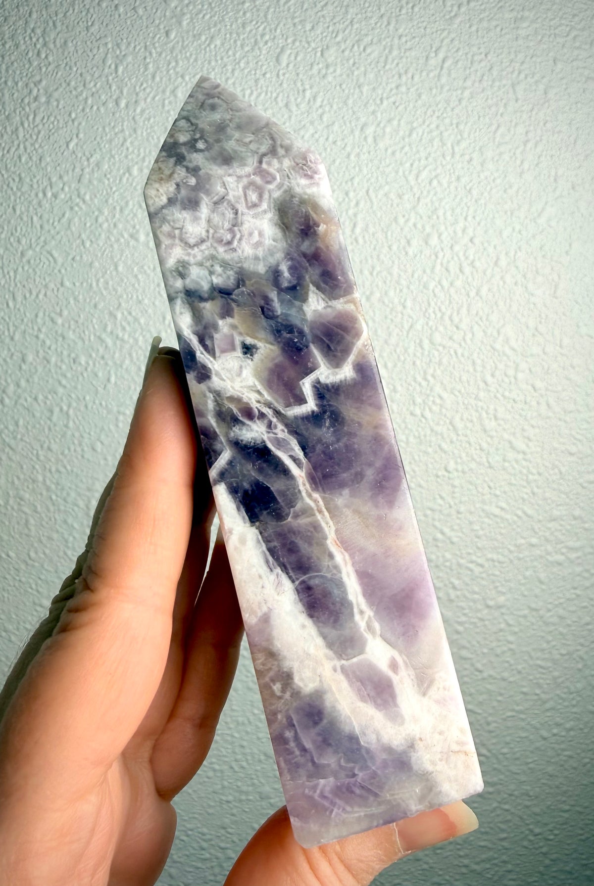 Chevron Amethyst crystal tower held in hand, revealing intricate zigzag banding, deep violet inclusions and lavender quartz