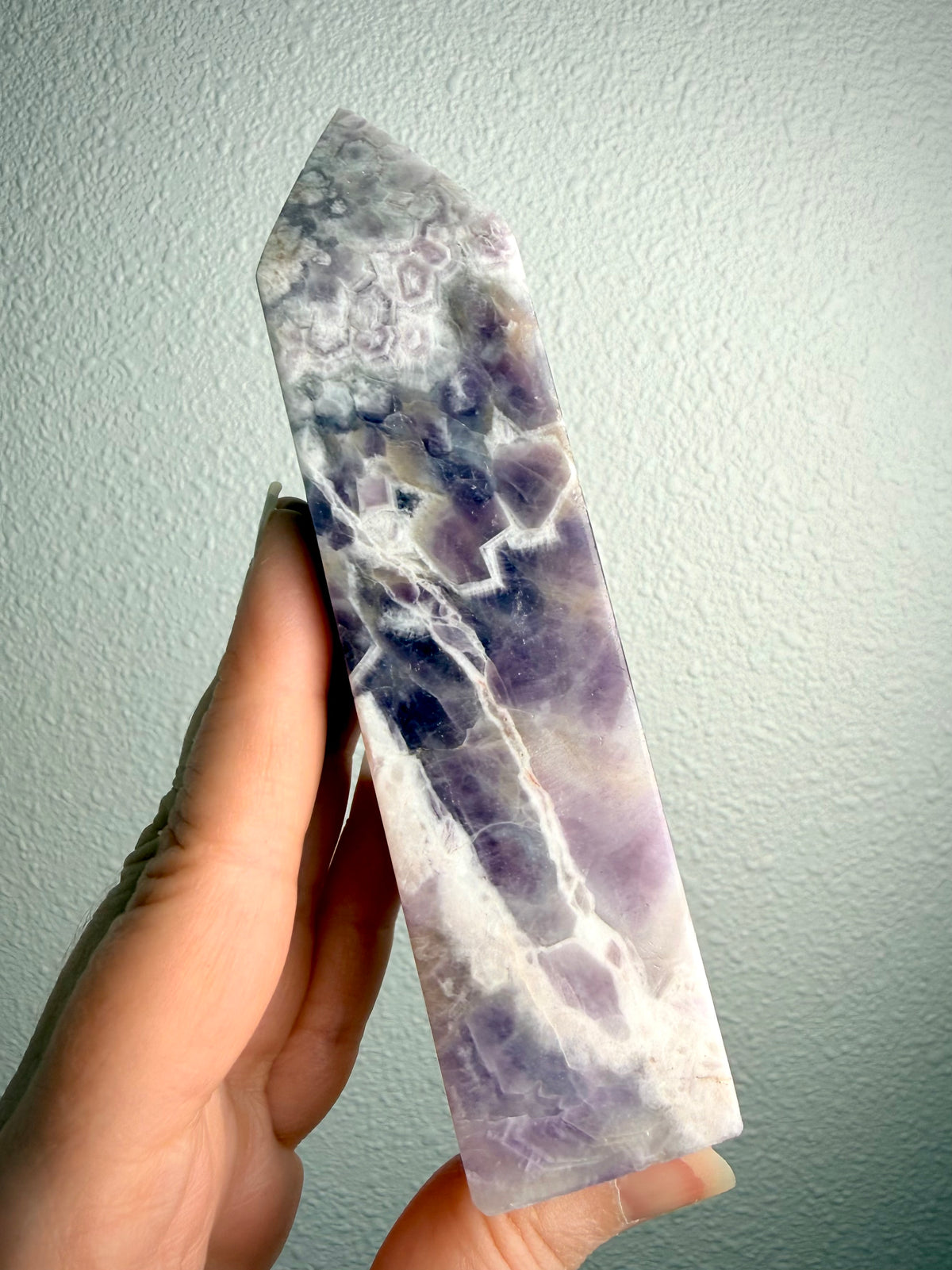 Chevron Amethyst crystal tower held in hand, revealing intricate zigzag banding, deep violet inclusions and lavender quartz