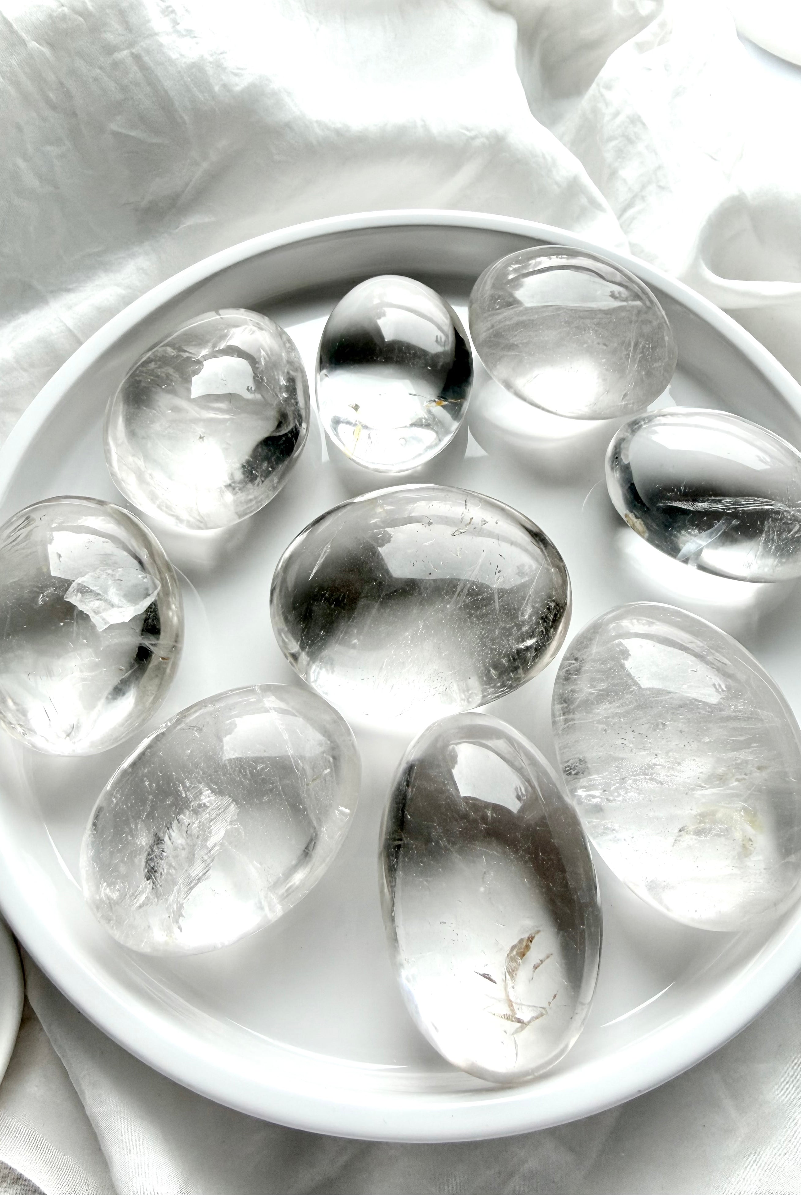 clear quartz palm stones arranged on white tray showing high clarity, natural inclusions, and polished finish
