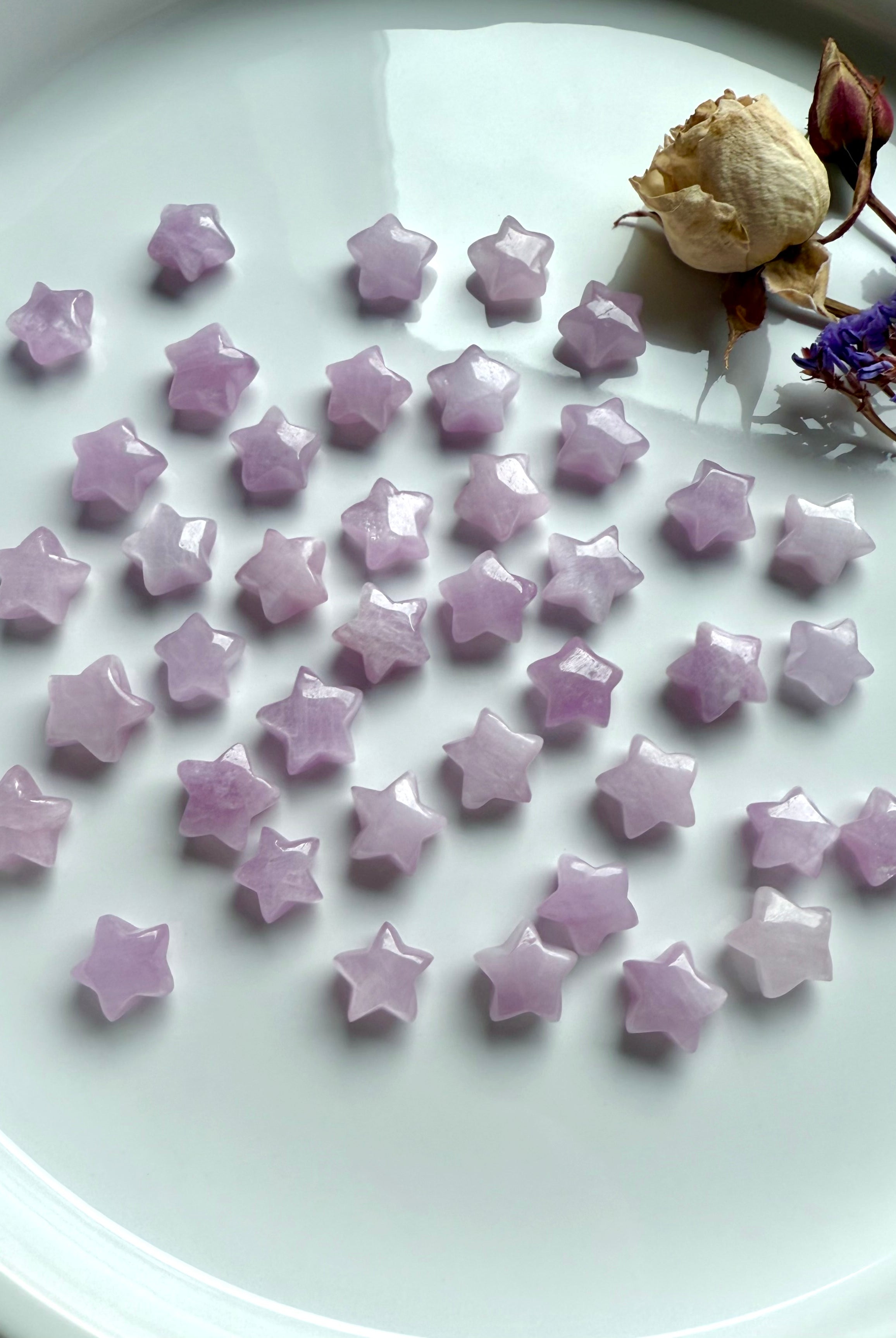Flat lay of glossy pink Kunzite mini stars with dried rose and purple statice flowers — high-vibe heart chakra altar decor.