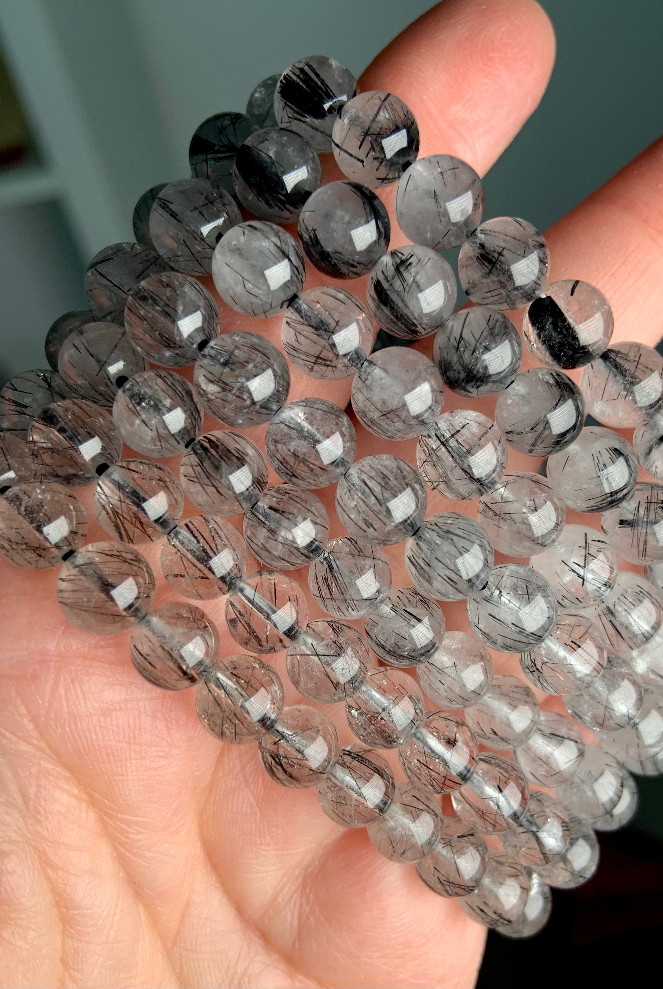 Stack of polished Tourmalinated Quartz bracelets in 7–8mm and 8–9mm beads, showing size variation and striking black rutile inclusions in clear quartz