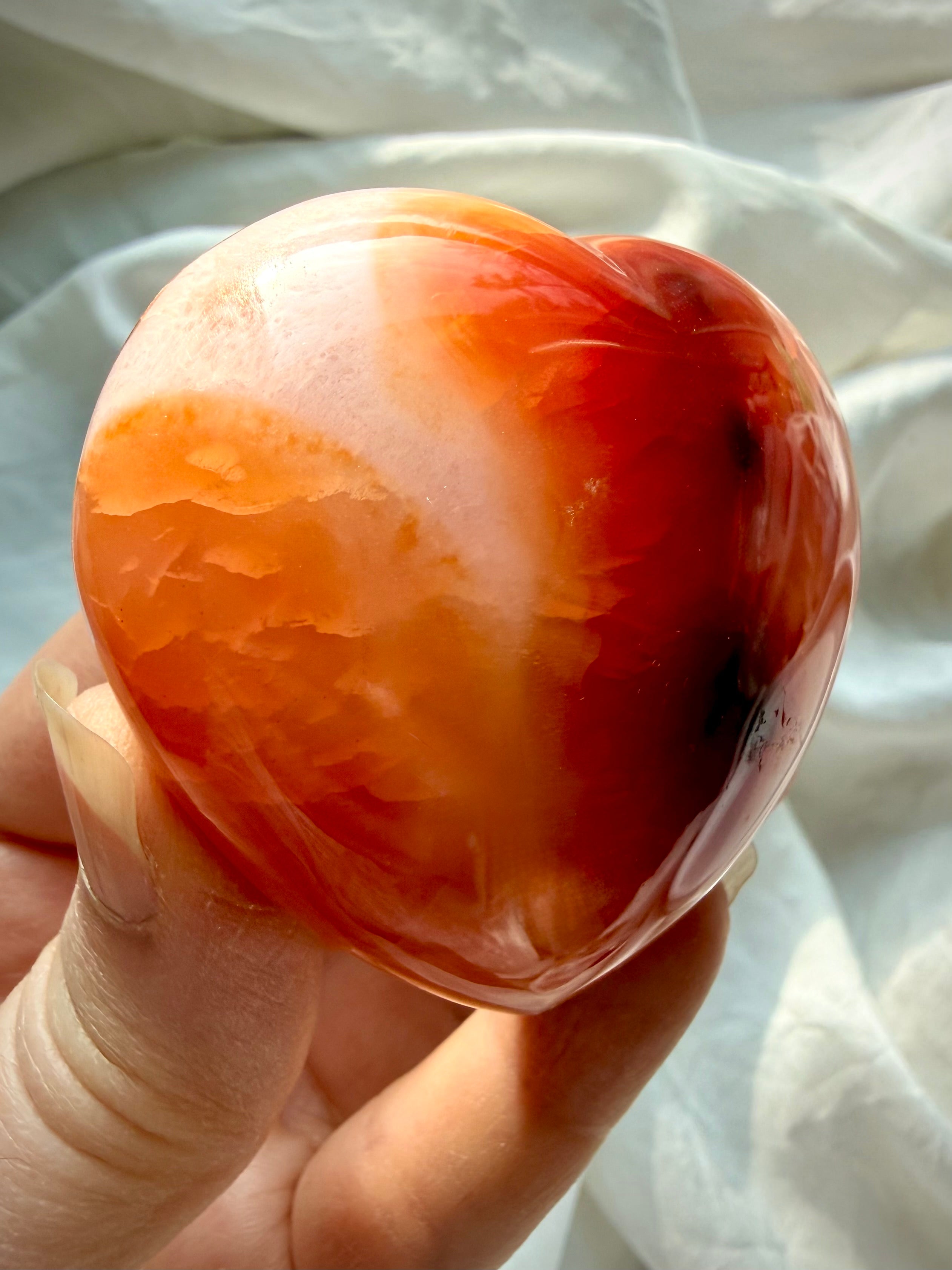Carnelian heart crystal held in hand showing rich red and orange translucency, glossy polish, and natural patterning for Sacral Chakra energy