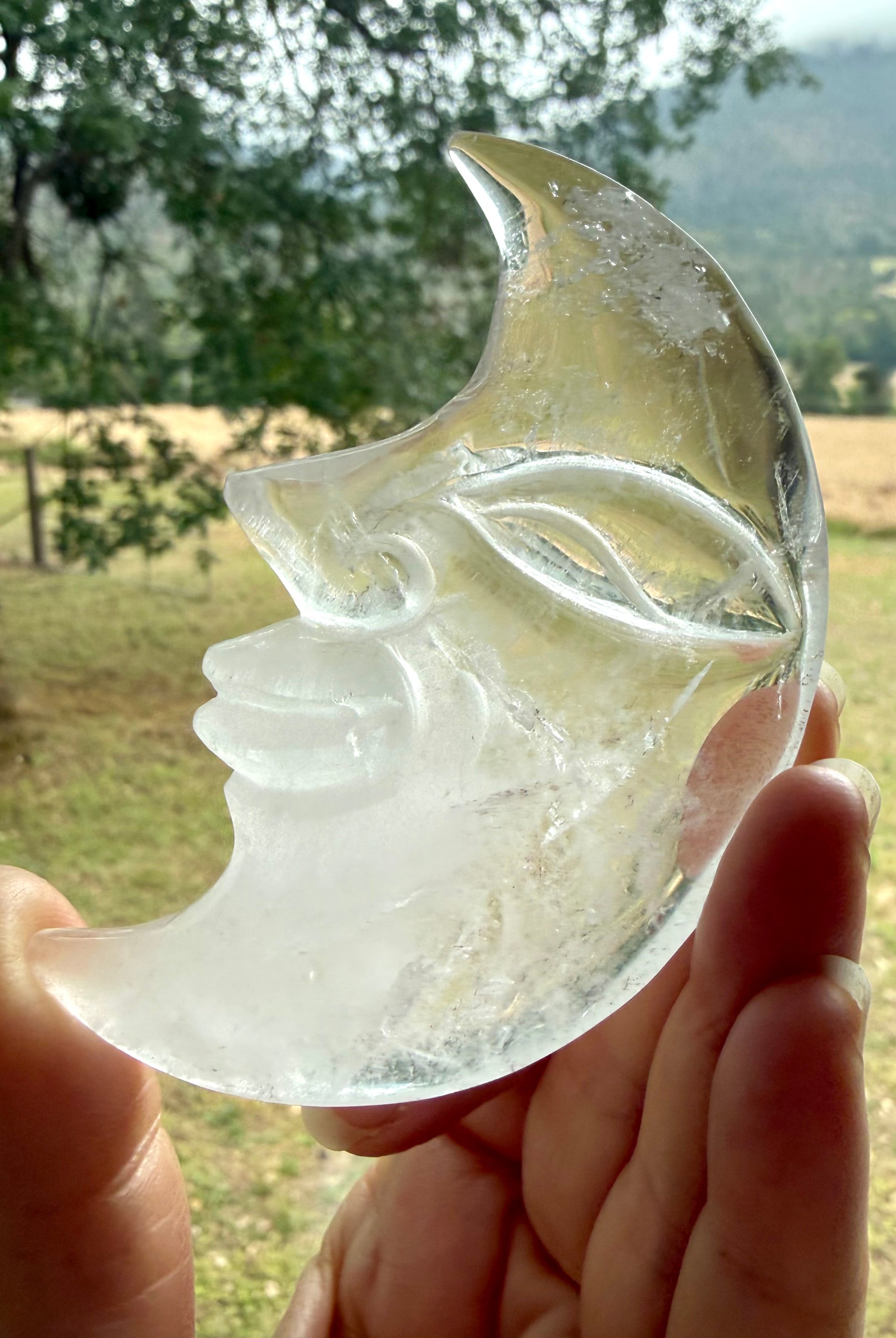 One-of-a-kind Clear Quartz Moon Face carving with a landscape in the background, highlighting clarity, internal patterns, and polished crystal beauty