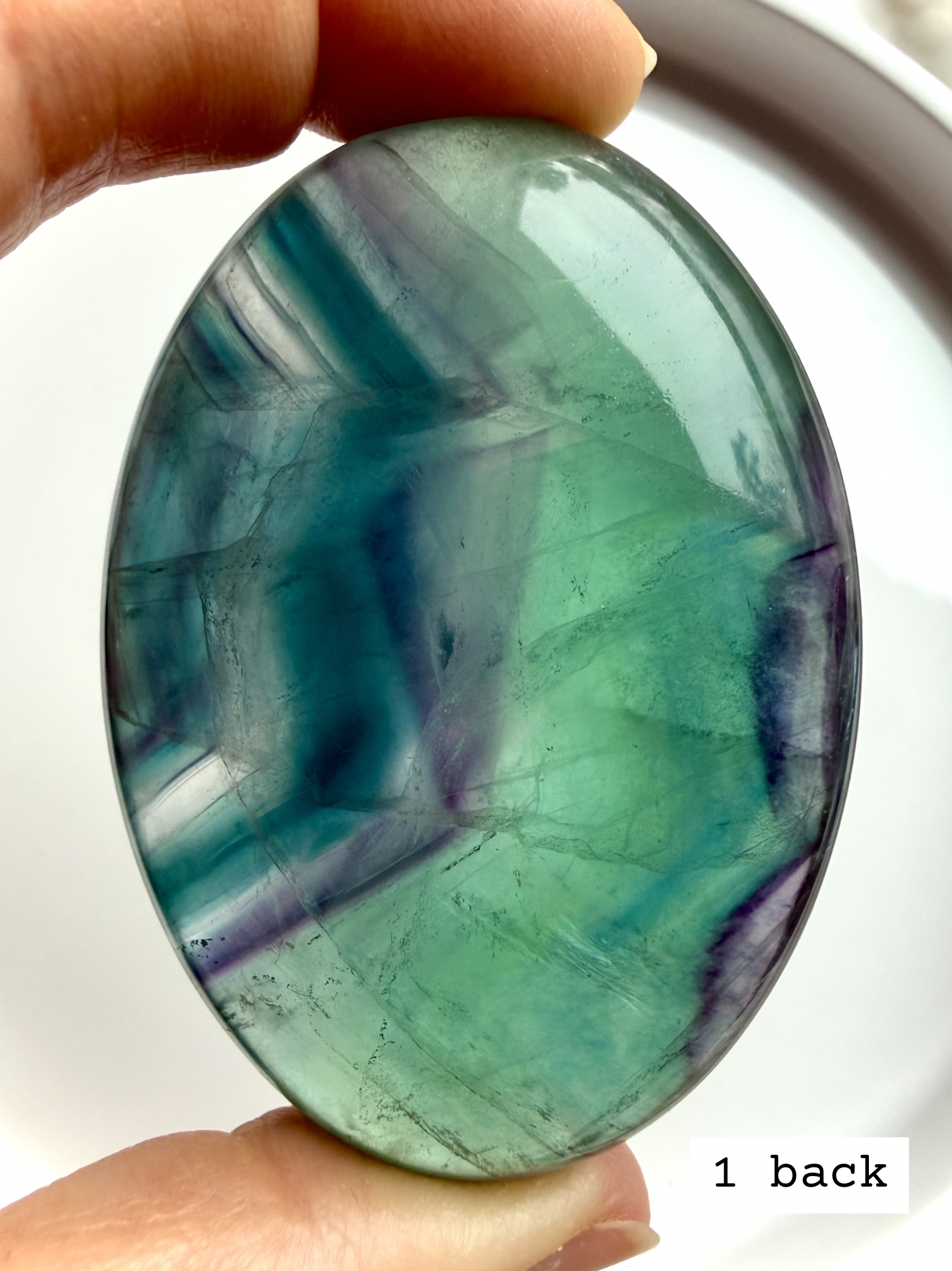 Teal fluorite palm stone #1 back view held to the light, revealing natural blue green layers and internal movement