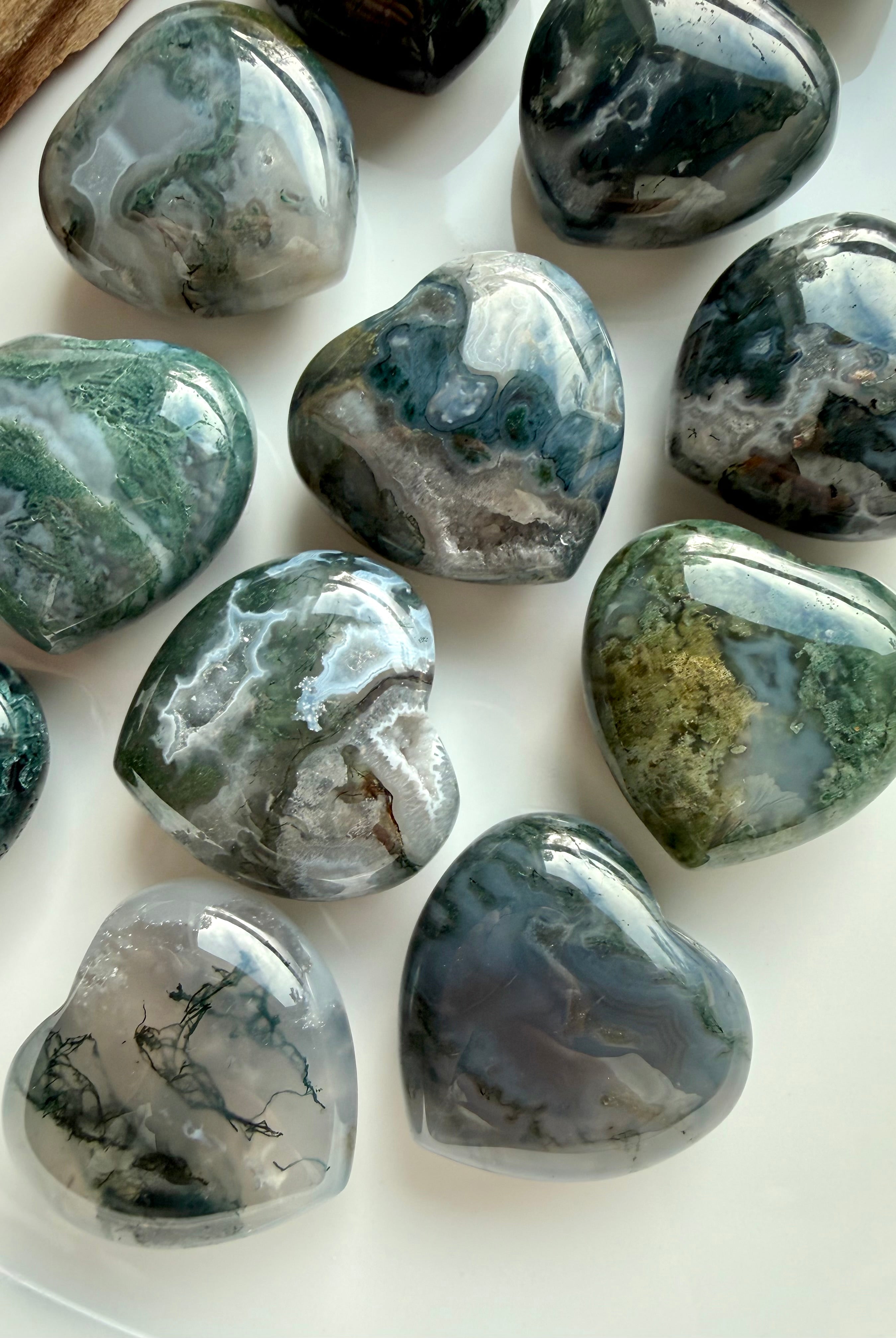 Natural Moss Agate heart crystals with swirling green, grey, and white mineral patterns on a white background