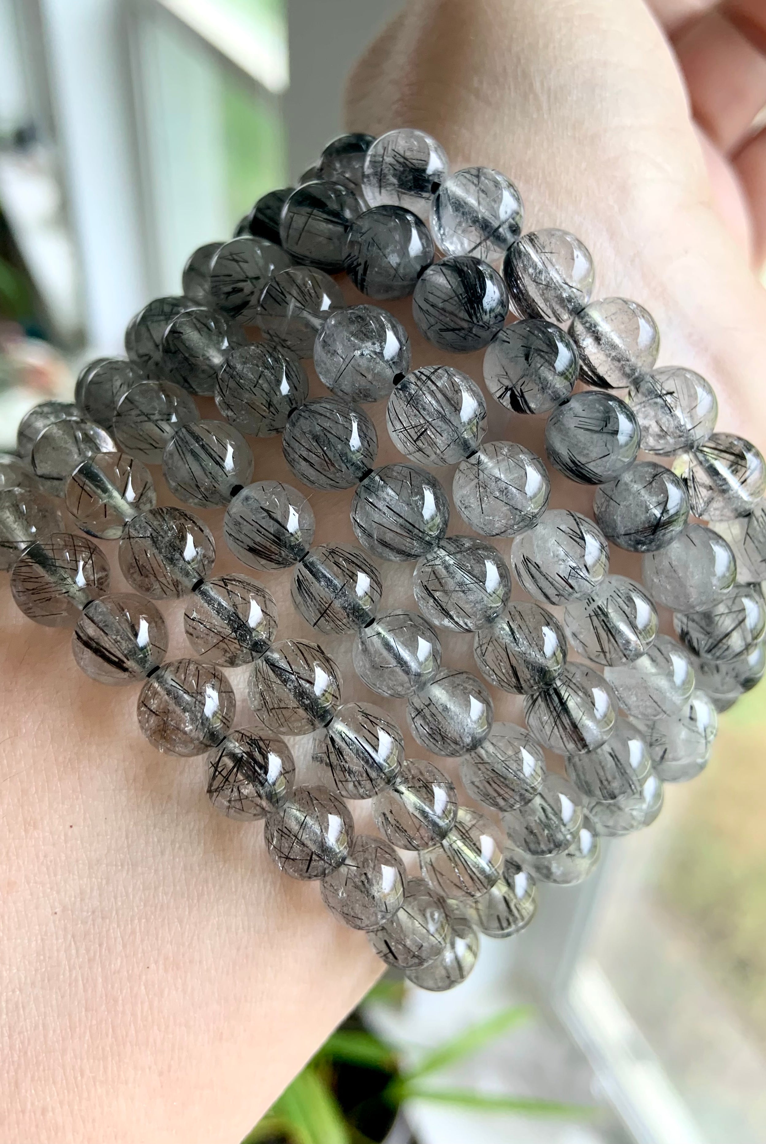 Angled shot of a stack of Tourmalinated Quartz bracelets on a wrist, displaying polished beads and dark rutile strands