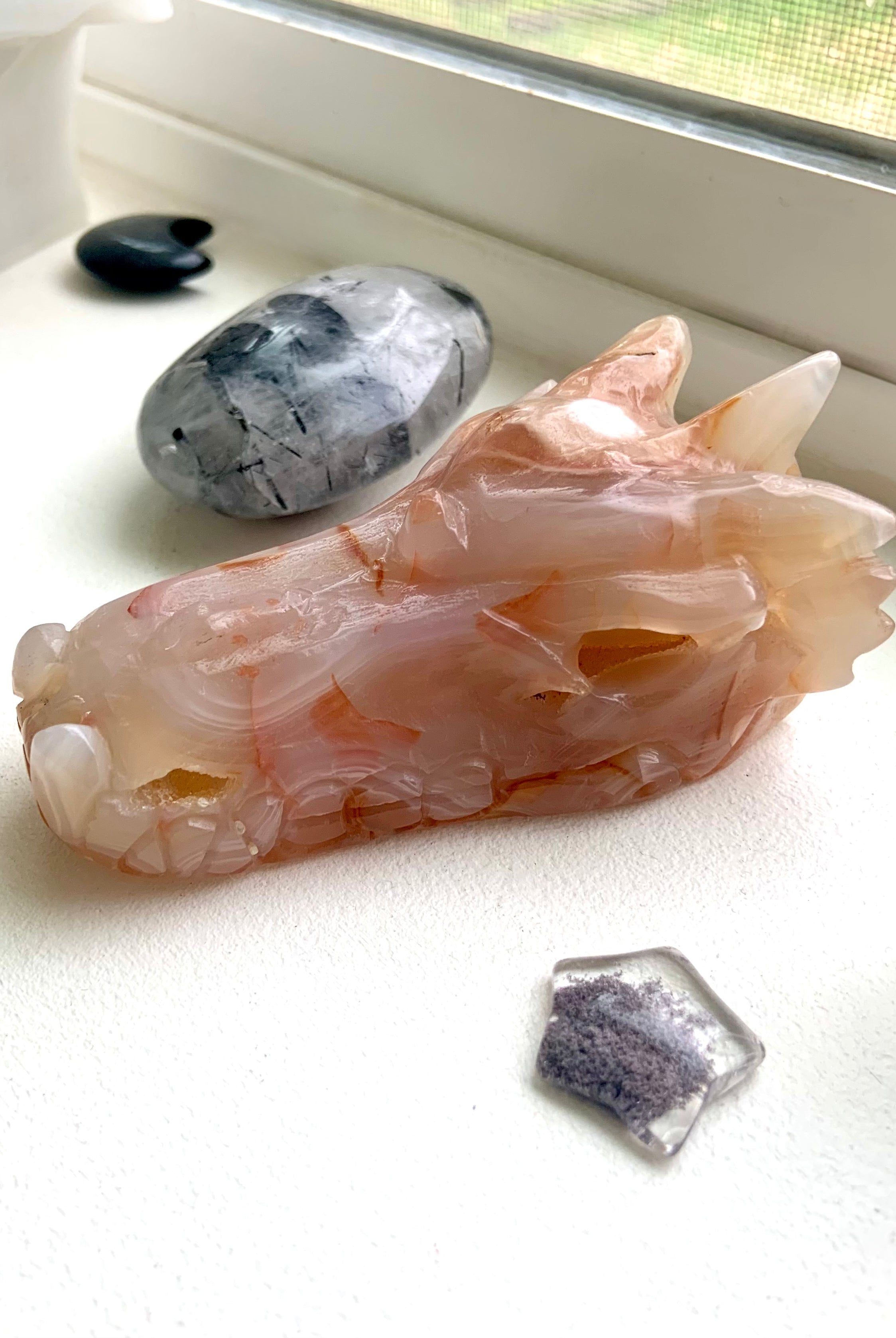 Carnelian Flower Agate Dragon Head Carving photographed in natura light on a windowsill with some other crystals