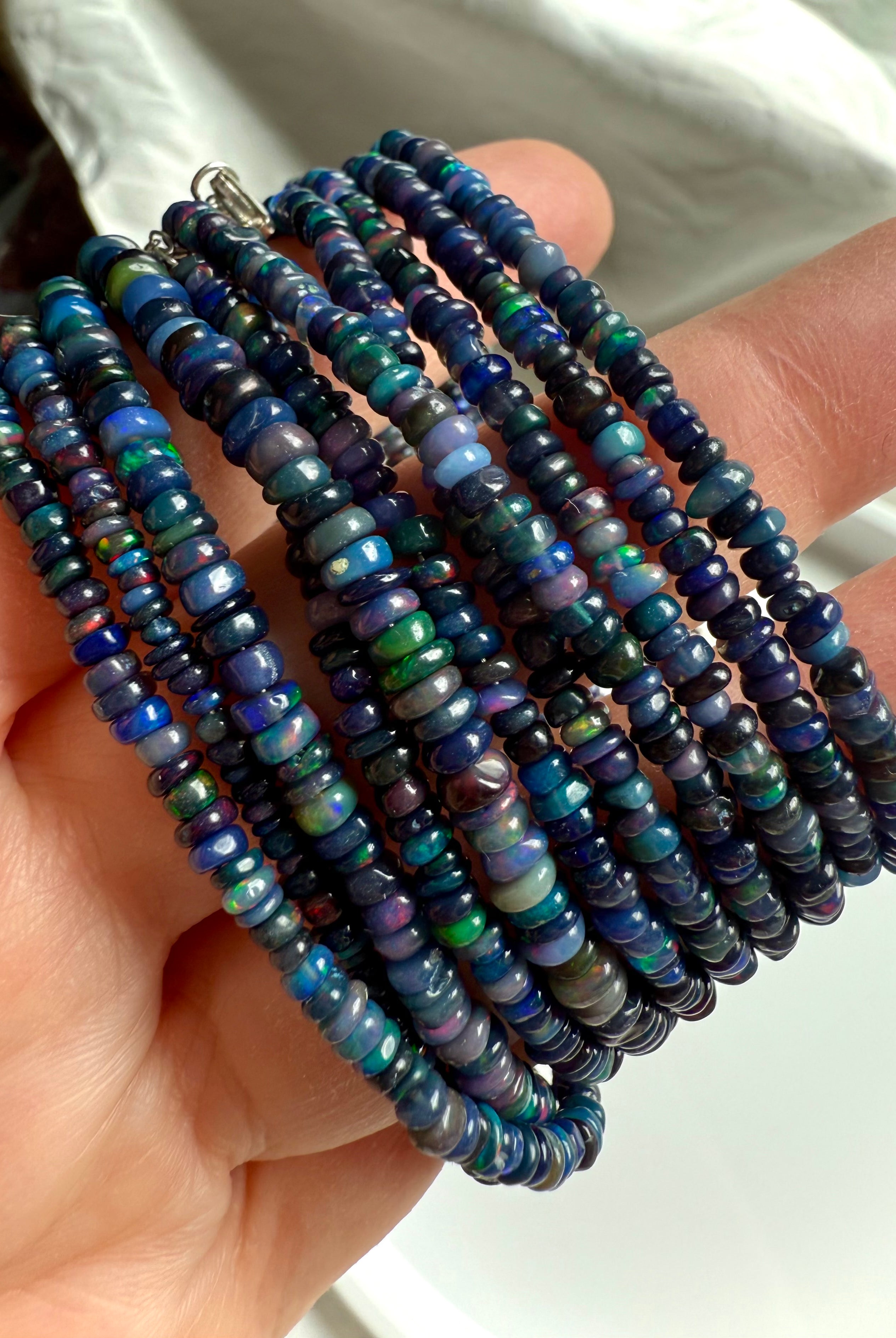 Close-up of multiple Black Fire Opal bracelets in different bead sizes shown at an angle — Ethiopian opal jewelry with fiery blue iridescence.