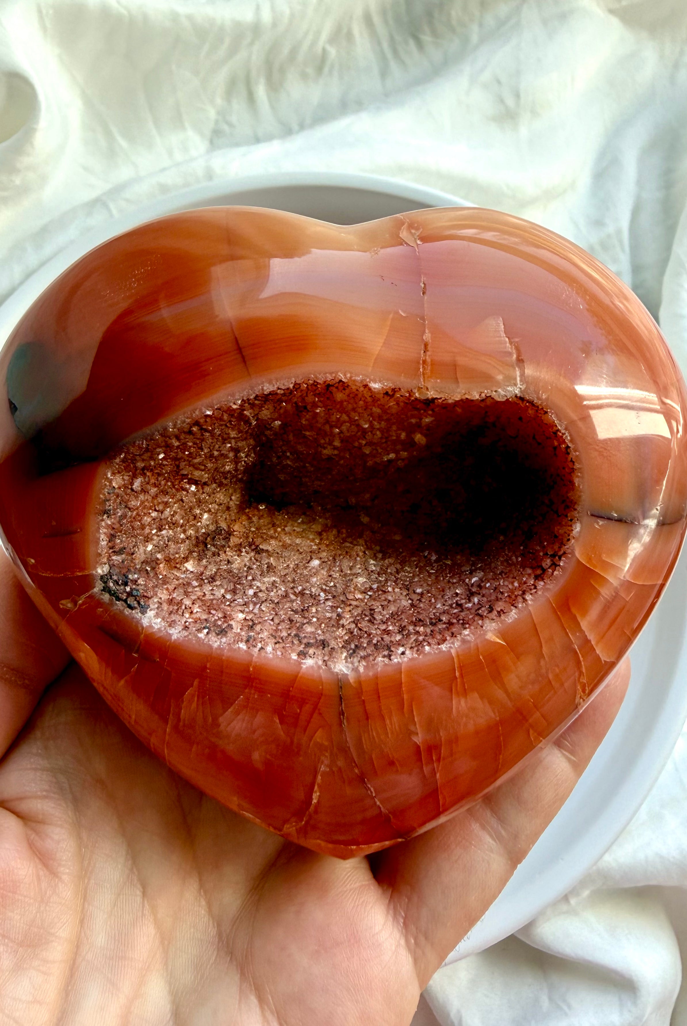 Large Carnelian geode heart held in hand highlighting sparkling druzy crystal cavity and polished natural banding