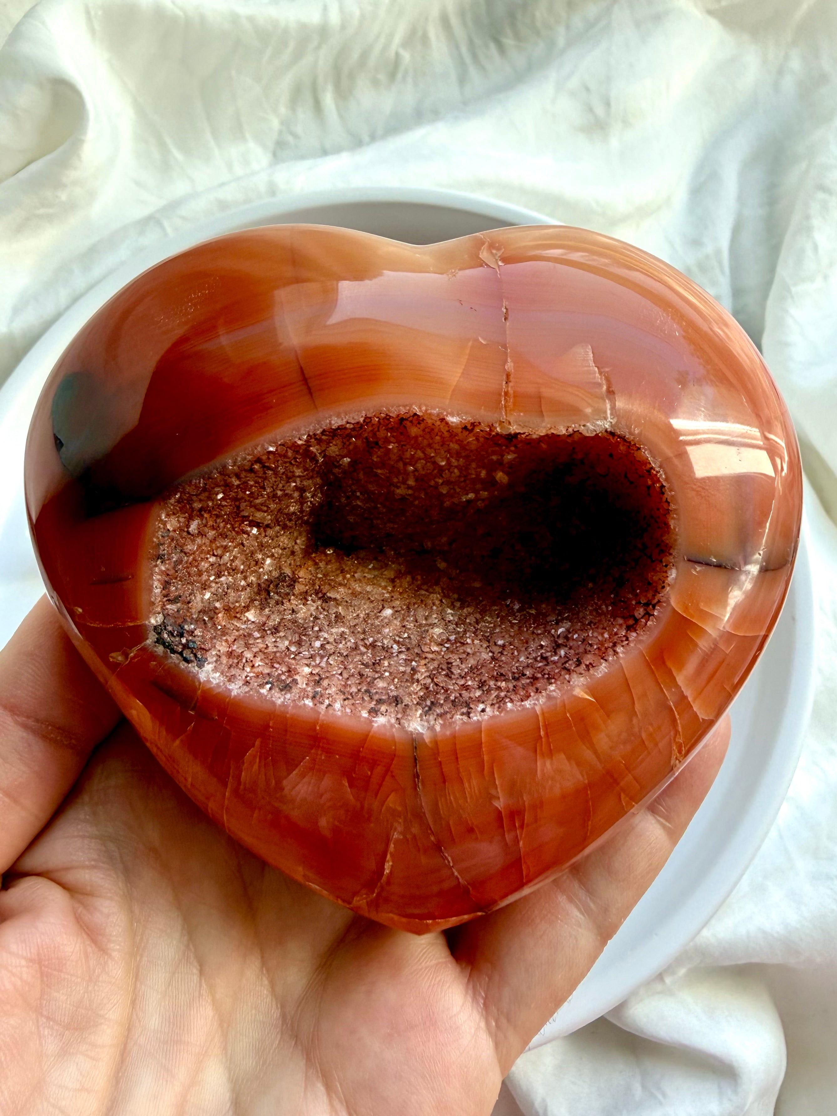 Large Carnelian geode heart held in hand highlighting sparkling druzy crystal cavity and polished natural banding