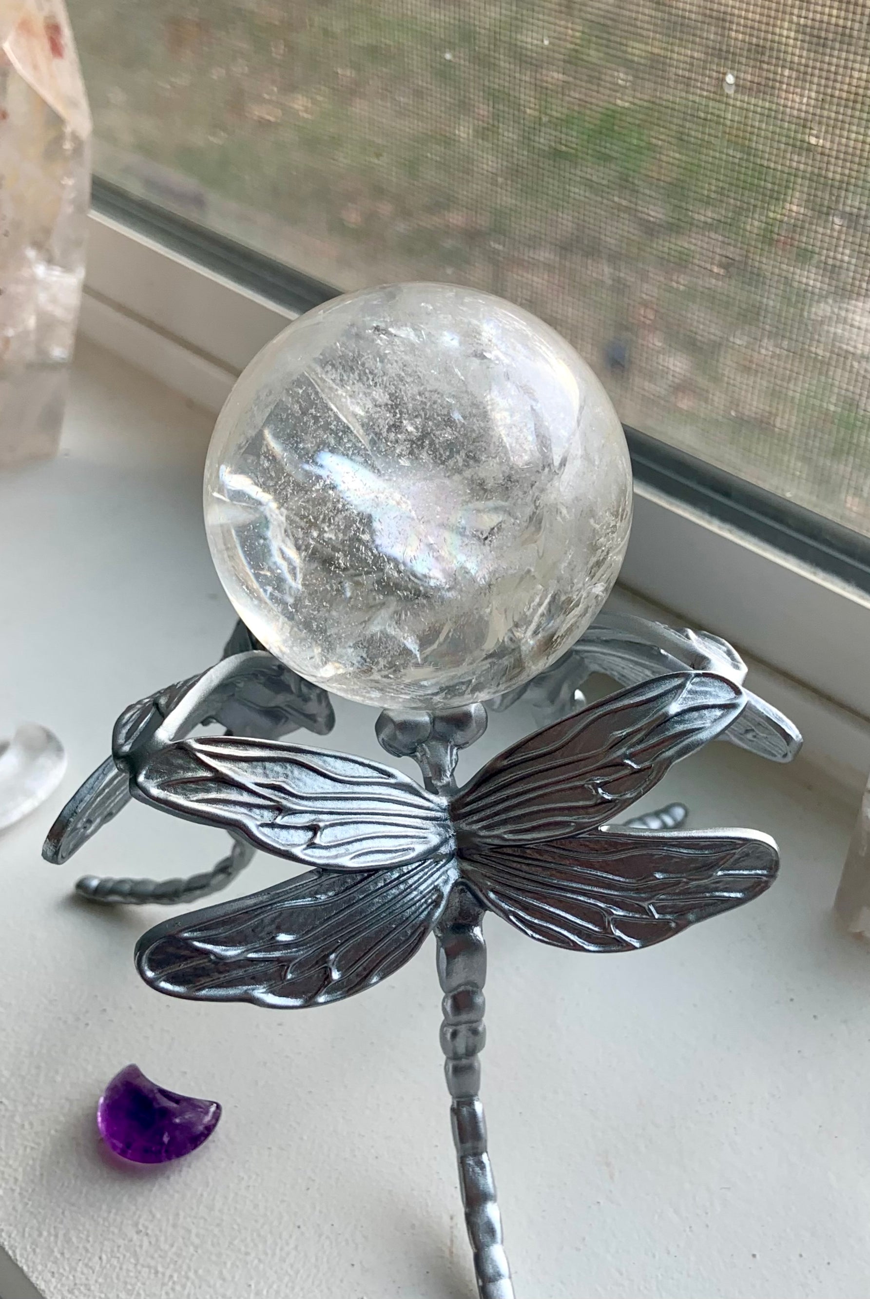Lifestyle image: silver dragonfly sphere holder with clear quartz crystal ball sitting on a windowsill.