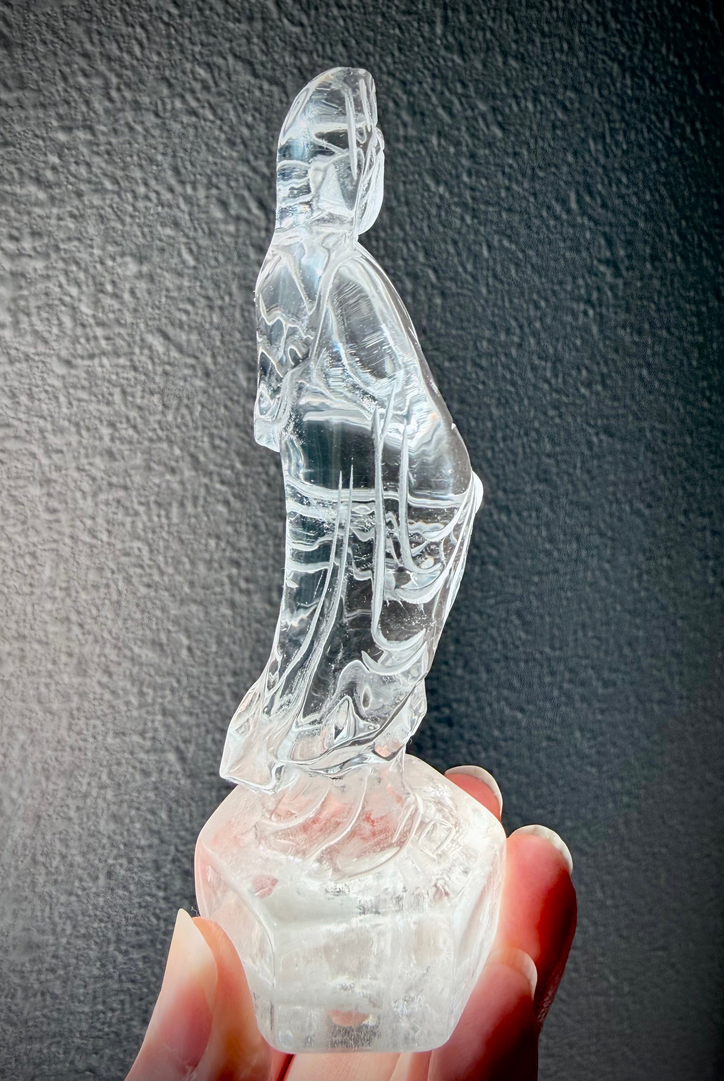 Side view of hand-carved Clear Quartz Quan Yin Goddess of Compassion statue with radiant transparency