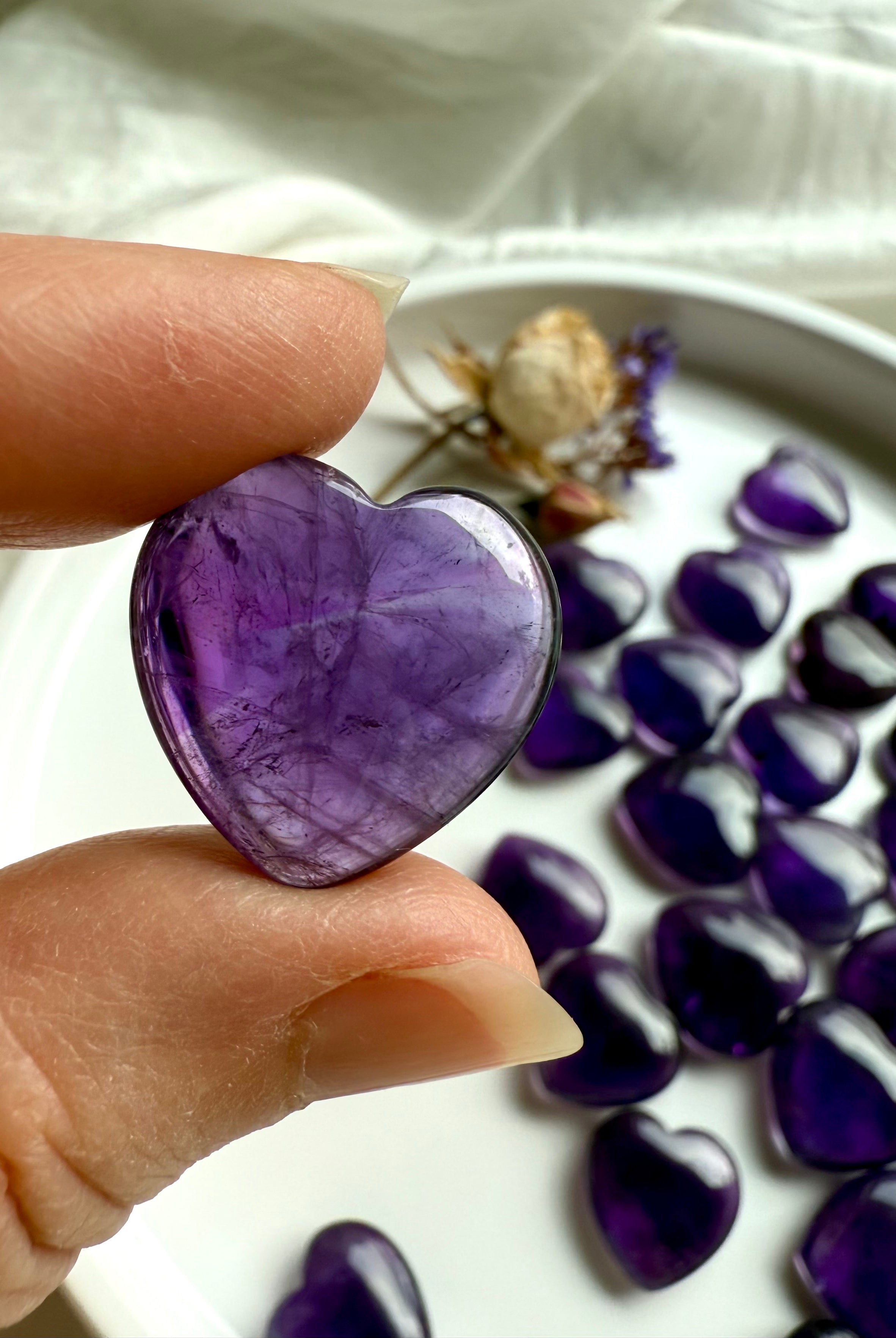 Close-up of an Amethyst crystal heart held gently between fingers, highlighting its violet translucence — a soothing crown chakra stone for inner wisdom and divine guidance.