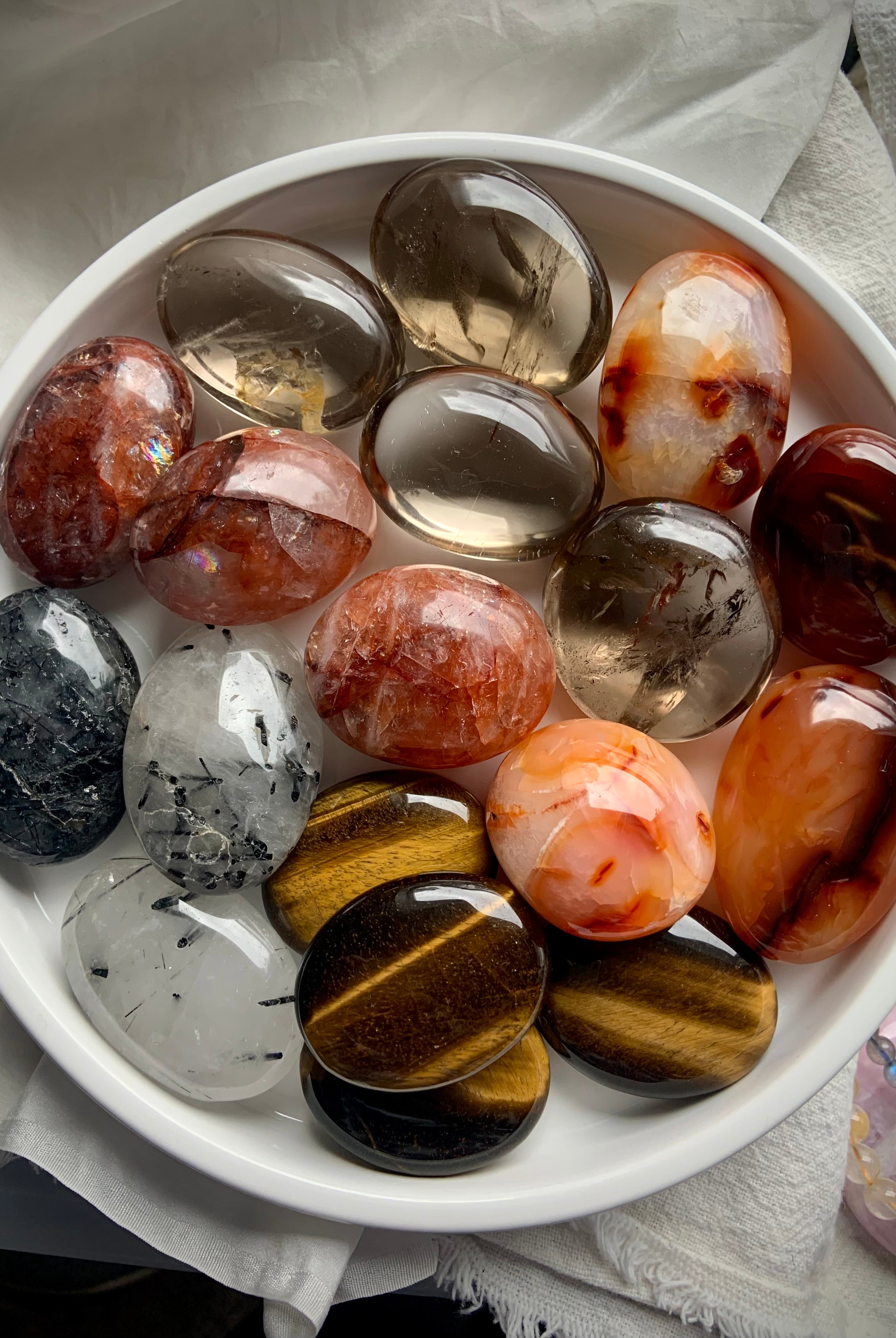 Overhead view of chakra crystal palm stones on a white plate — shows size, shape & color variety in this grounding crystal set.