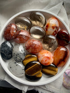 Overhead view of chakra crystal palm stones on a white plate — shows size, shape & color variety in this grounding crystal set.