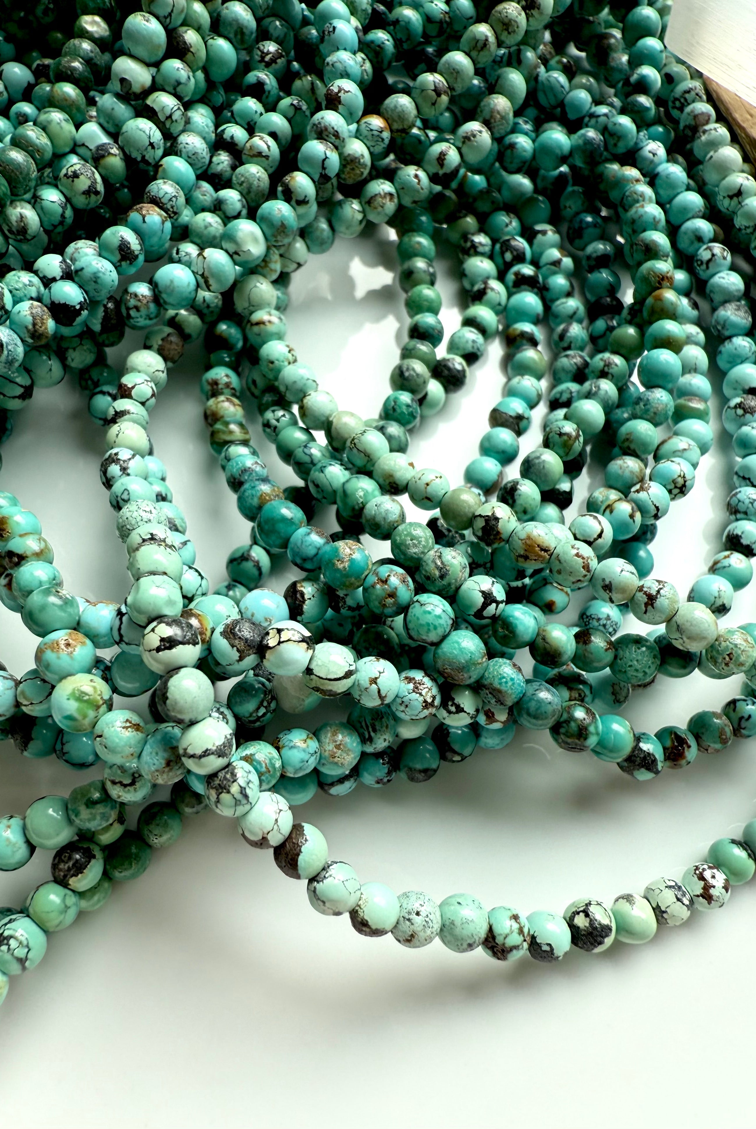 Tumbled pile of turquoise 4mm bead strands in shades of teal, mint, and aqua green