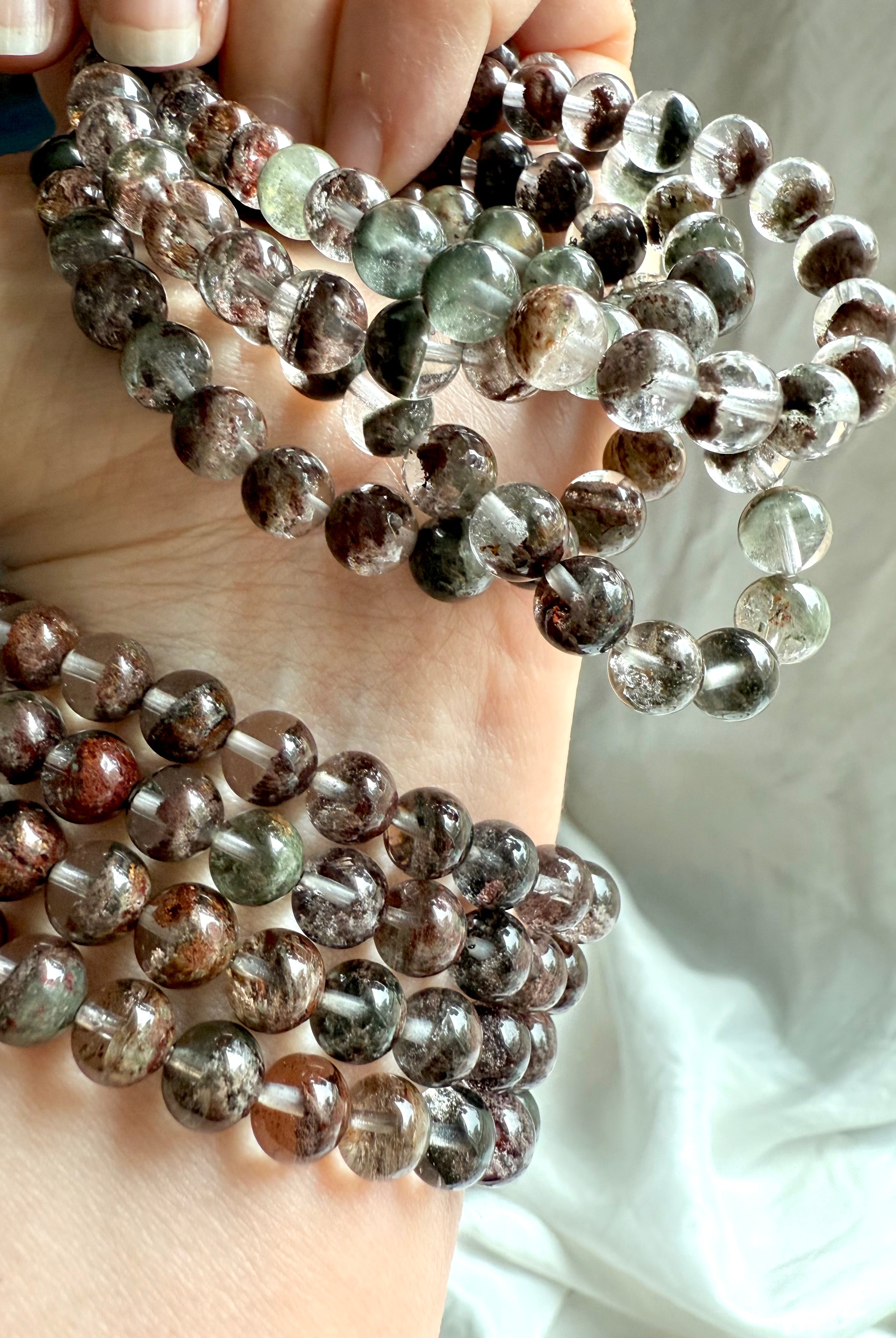 Close-up of Garden Quartz bracelet beads with mossy inclusions and earthy red-brown phantoms, hand model in soft light