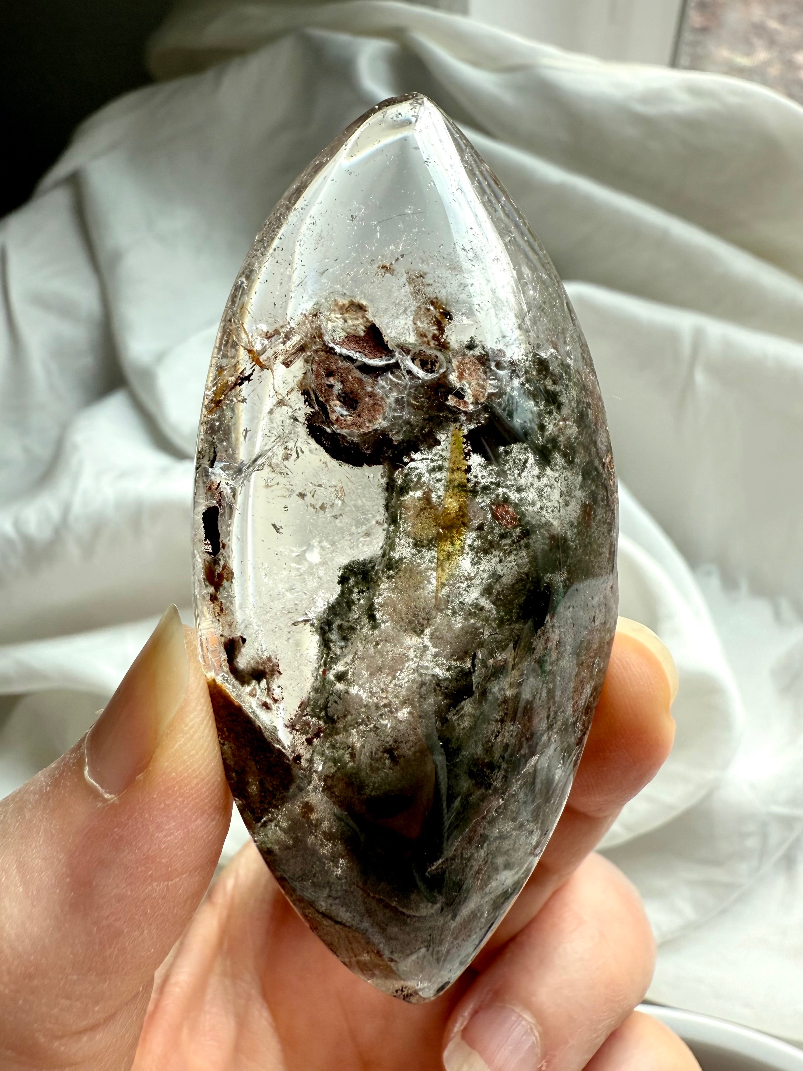 Hand-held Garden Quartz crystal lens with golden healer and mossy inclusions in natural daylight