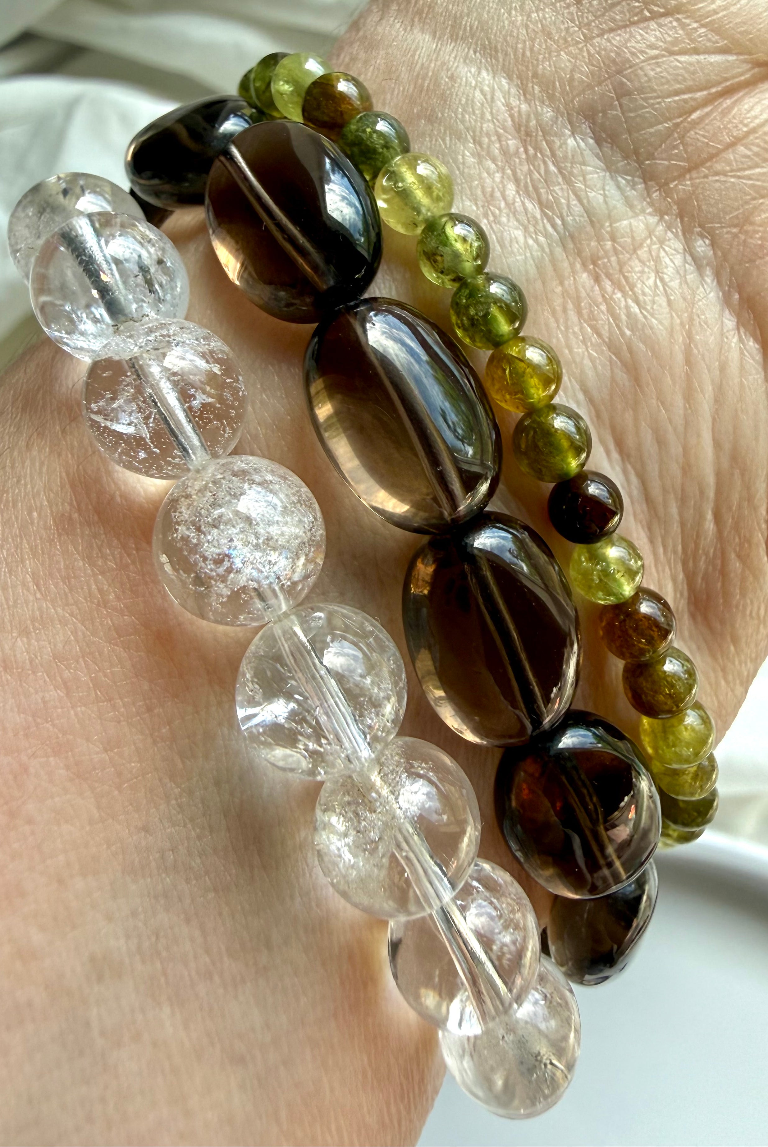Rainbow Quartz, Smoky Quartz, and Tsavorite Garnet bracelet stack with transparent crystal gemstones and earthy neutral tones