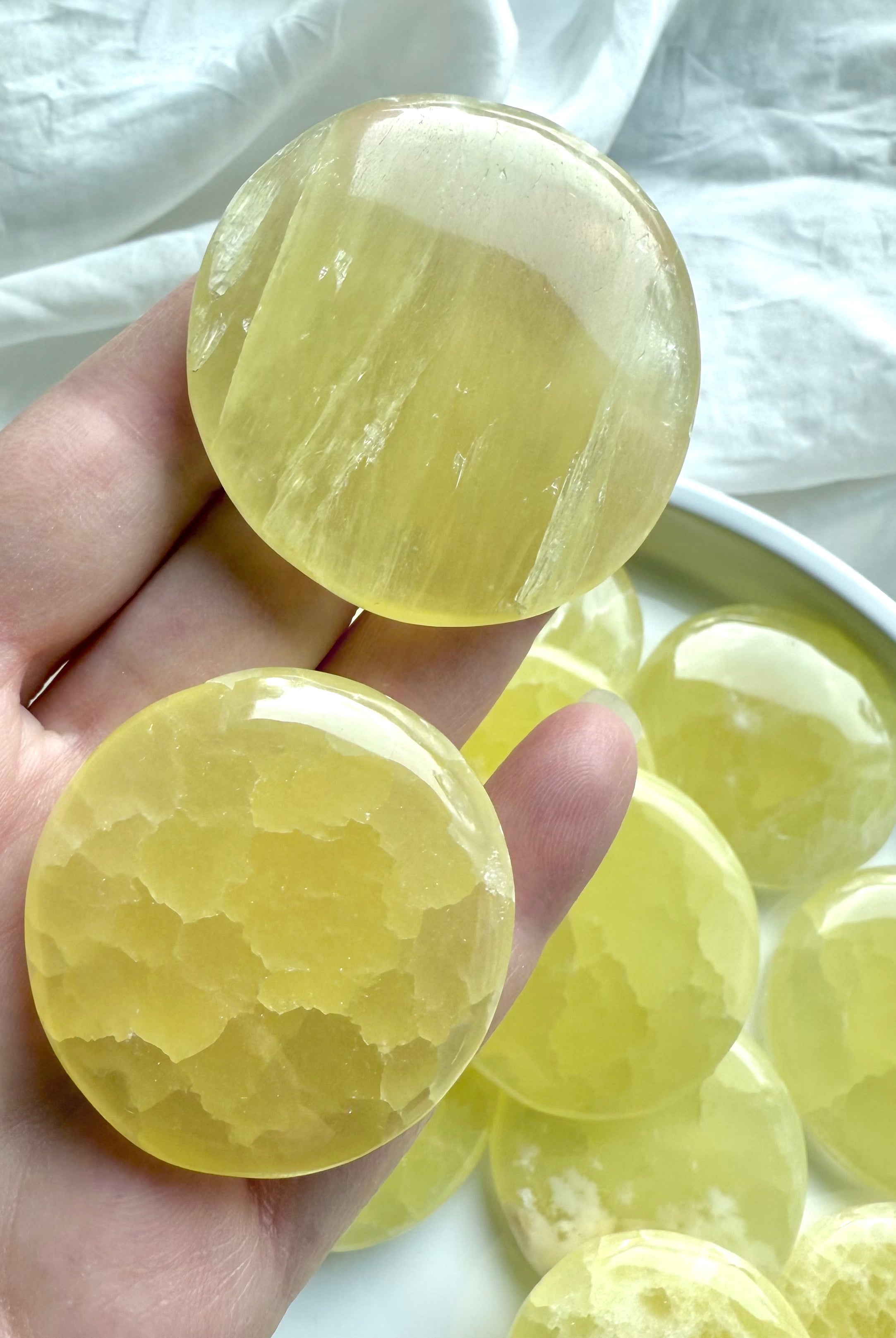 Hand holding two lemon calcite crystal discs showing smooth polish, natural texture, and vibrant color