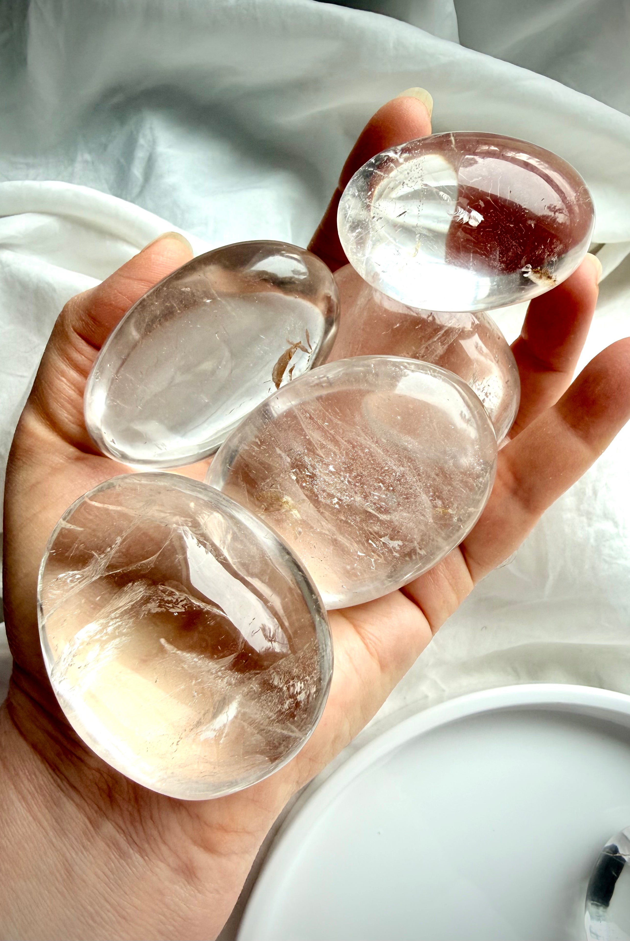 five clear quartz palm stones held in hand showing high clarity, natural inclusions, and polished finish