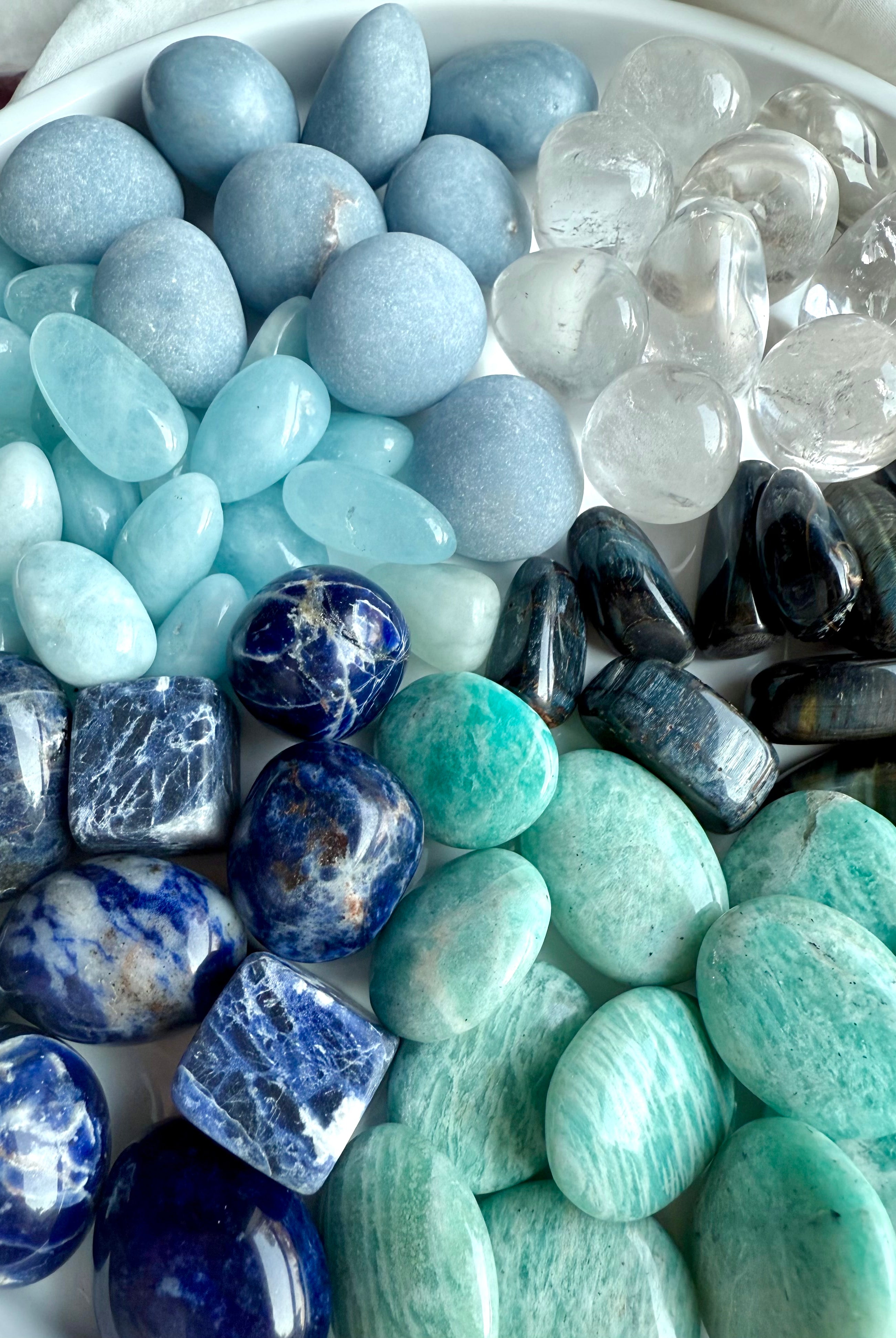 Close-up of Throat Chakra Crystal Set — Angelite, Sodalite, Amazonite, Aquamarine, Blue Tiger’s Eye, and Clear Quartz healing stones on white plate.