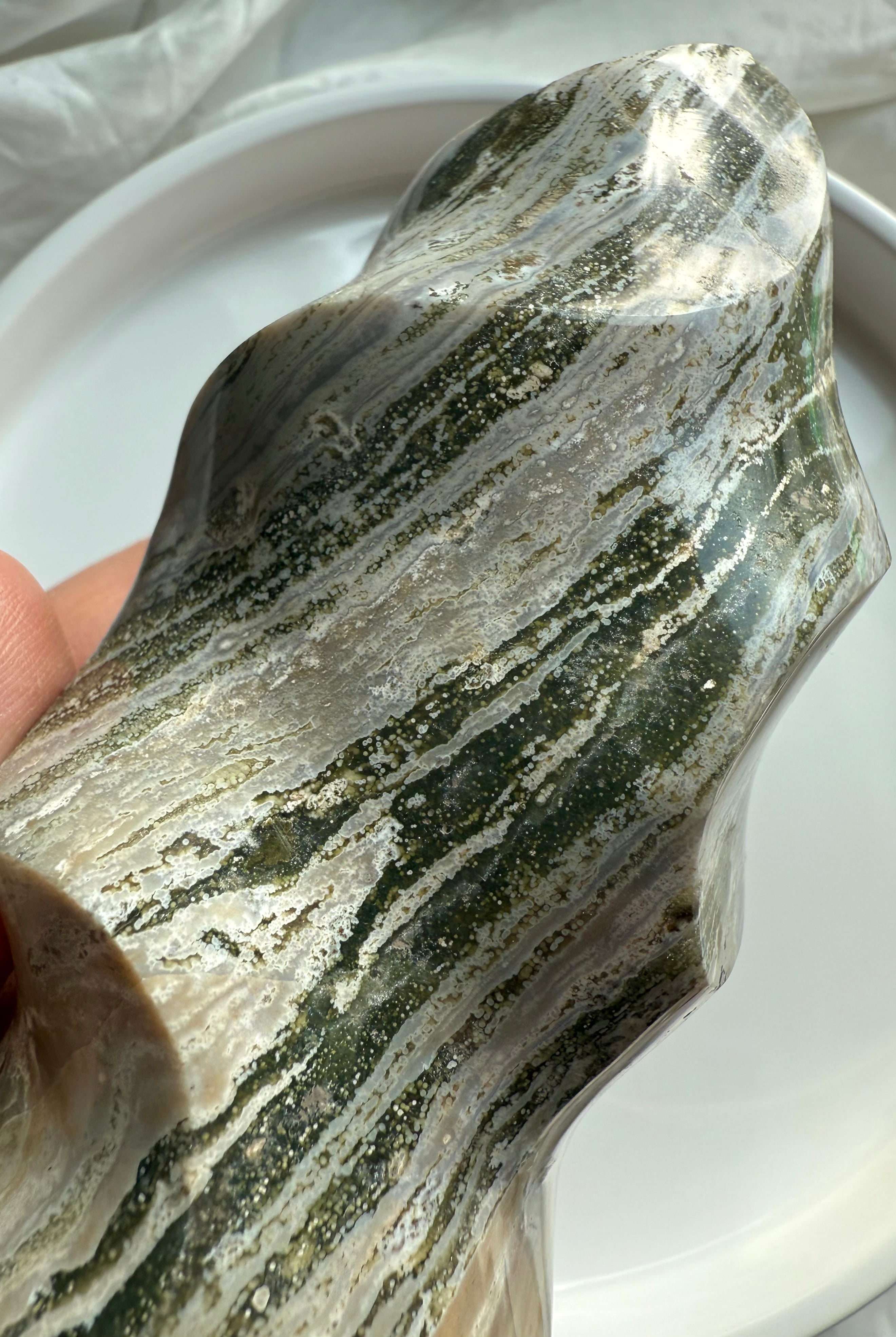 Close-up of Green Ocean Jasper’s intricate mossy striations and glossy carved surfaces in a freeform flame shape.
