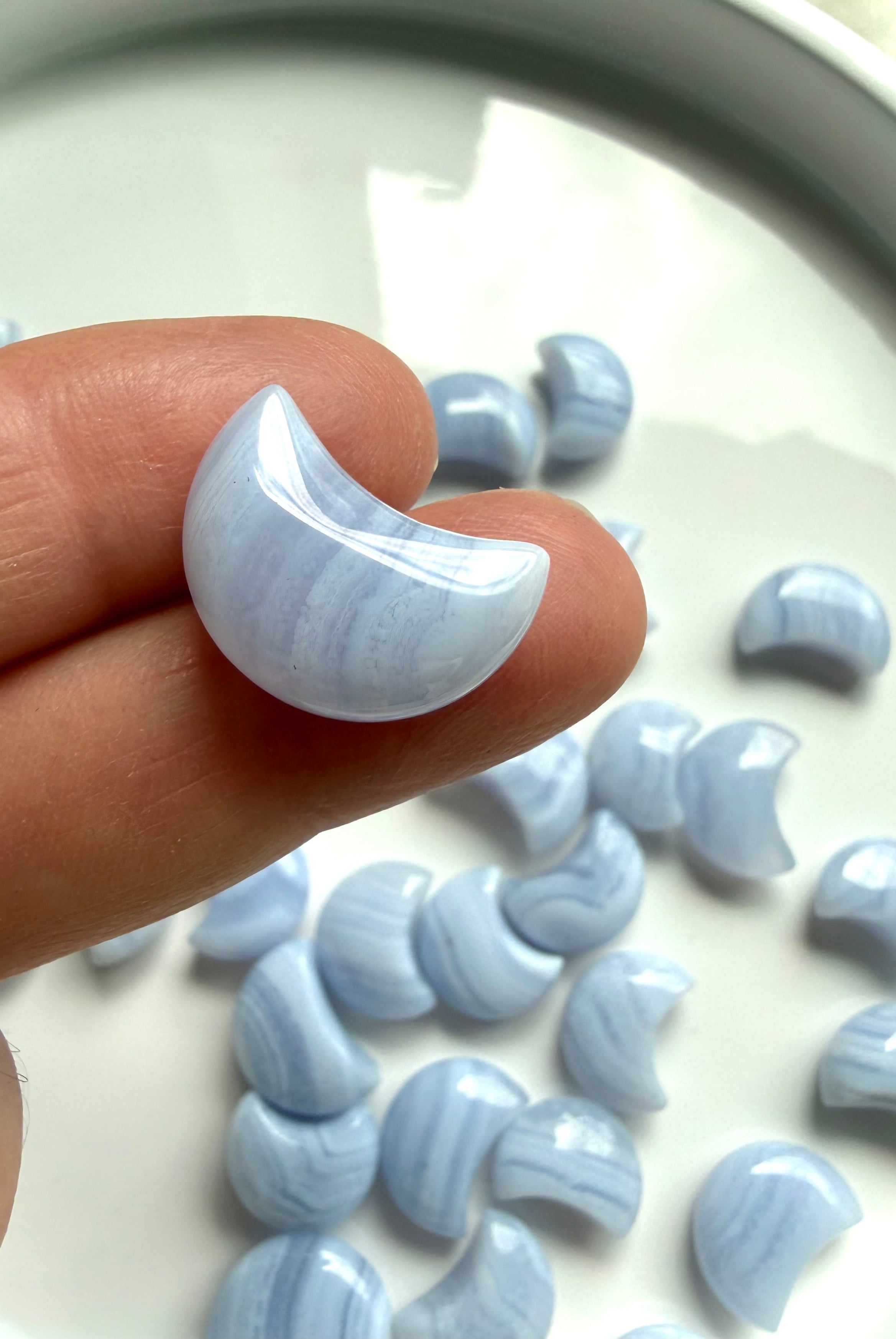 Small polished Blue Lace Agate crescent moon carving held between fingers to show detailed banding and size