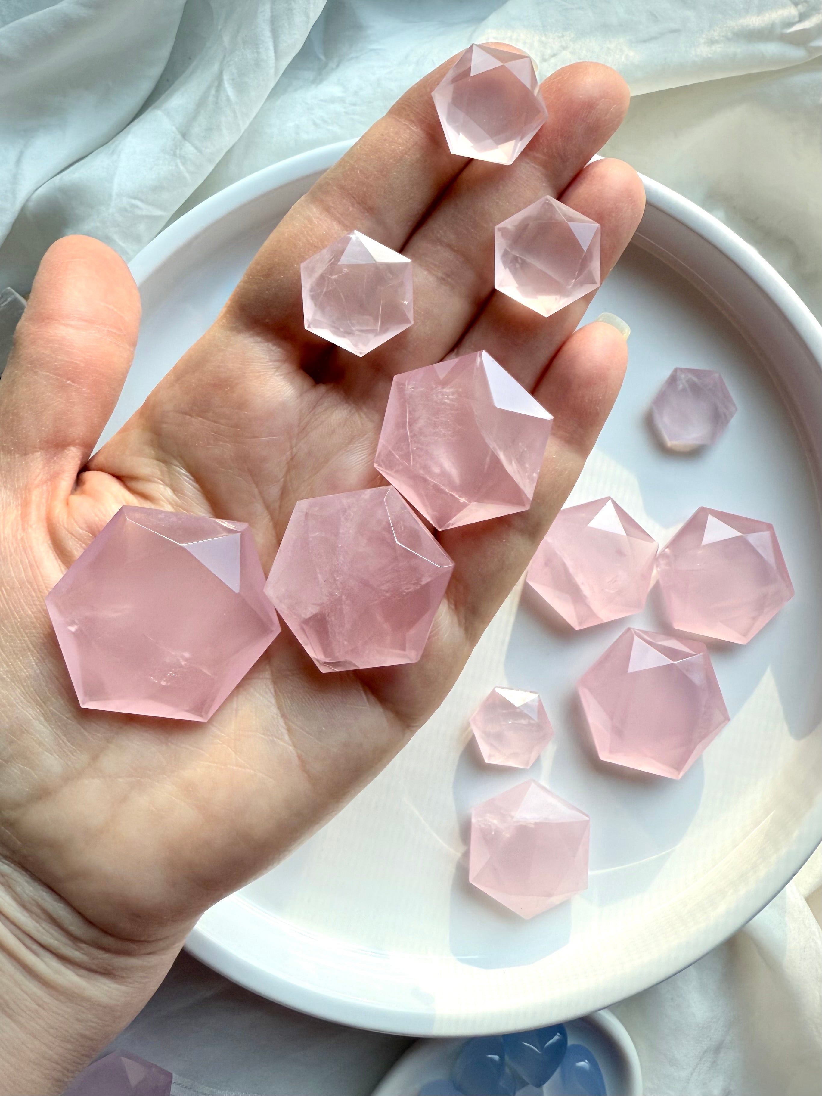 Hand holding assorted faceted rose quartz hexagons in small to large sizes, showing high quality polish, clarity, facets, and soft pink color.