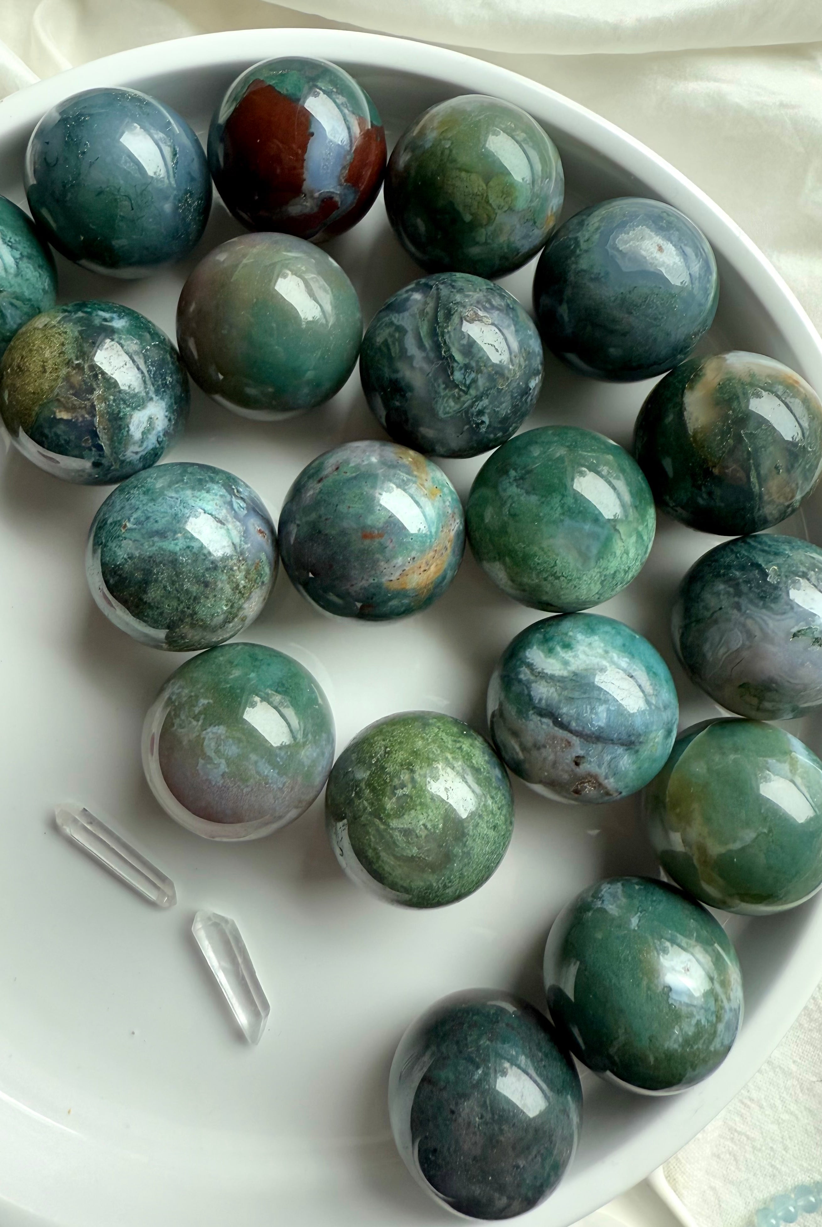 Colorful moss agate mini spheres shown on a white plate with some other crystals