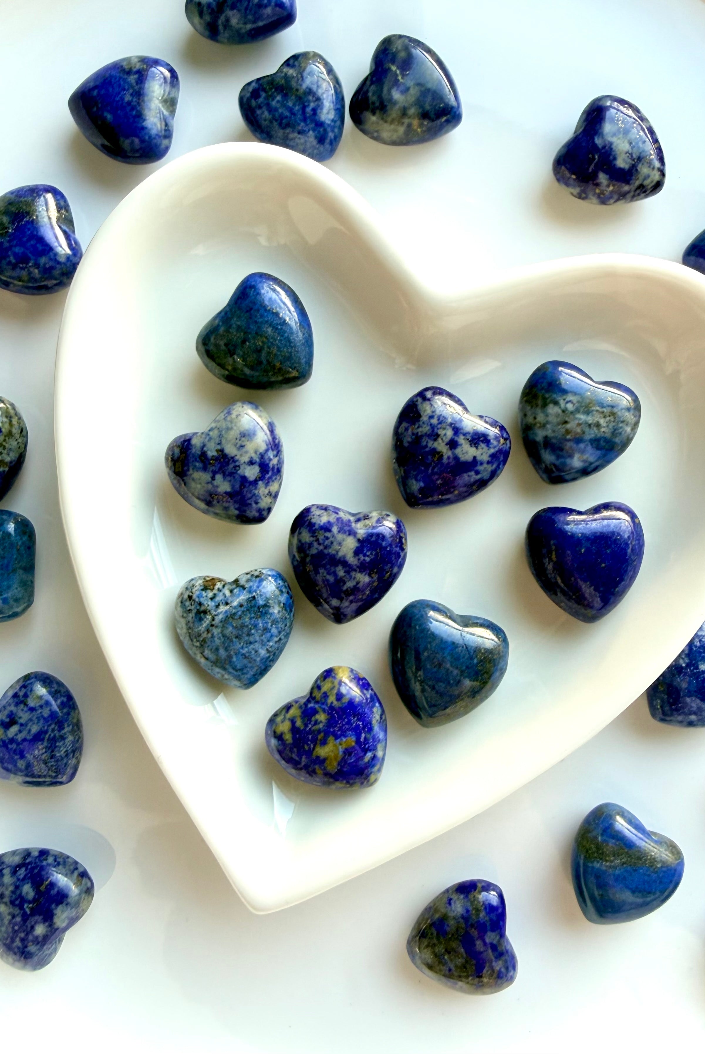 Assorted Mini Lapis Lazuli heart carvings displayed in a white heart dish, polished blue crystal hearts with natural pattern variation, each stone unique