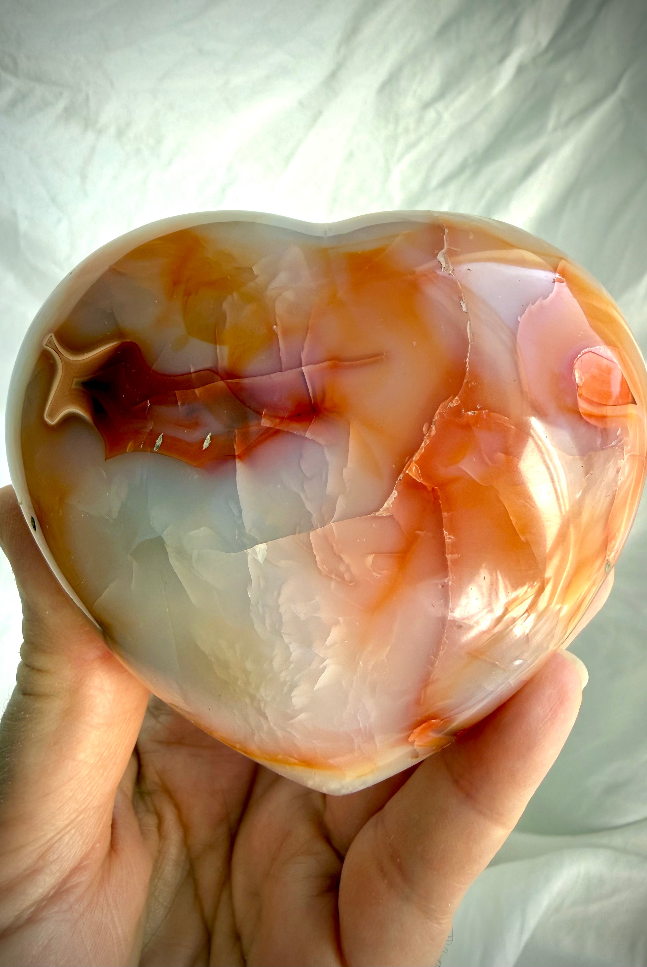 Carnelian heart crystal held in hand with vibrant orange banding and glossy polished finish for size reference