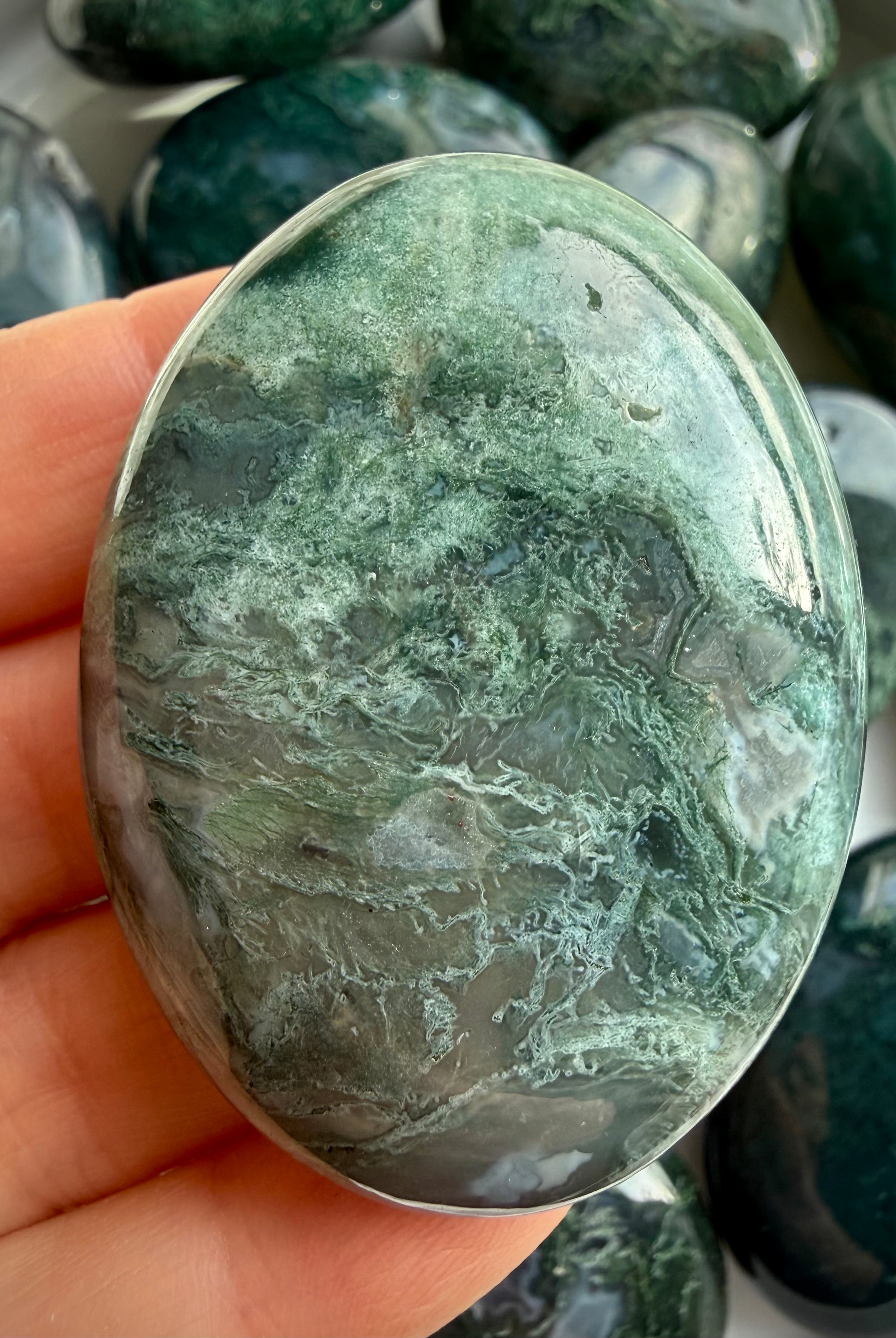 Close-up moss agate palm stone with translucent chalcedony and moss-like inclusions, soothing grounding crystal