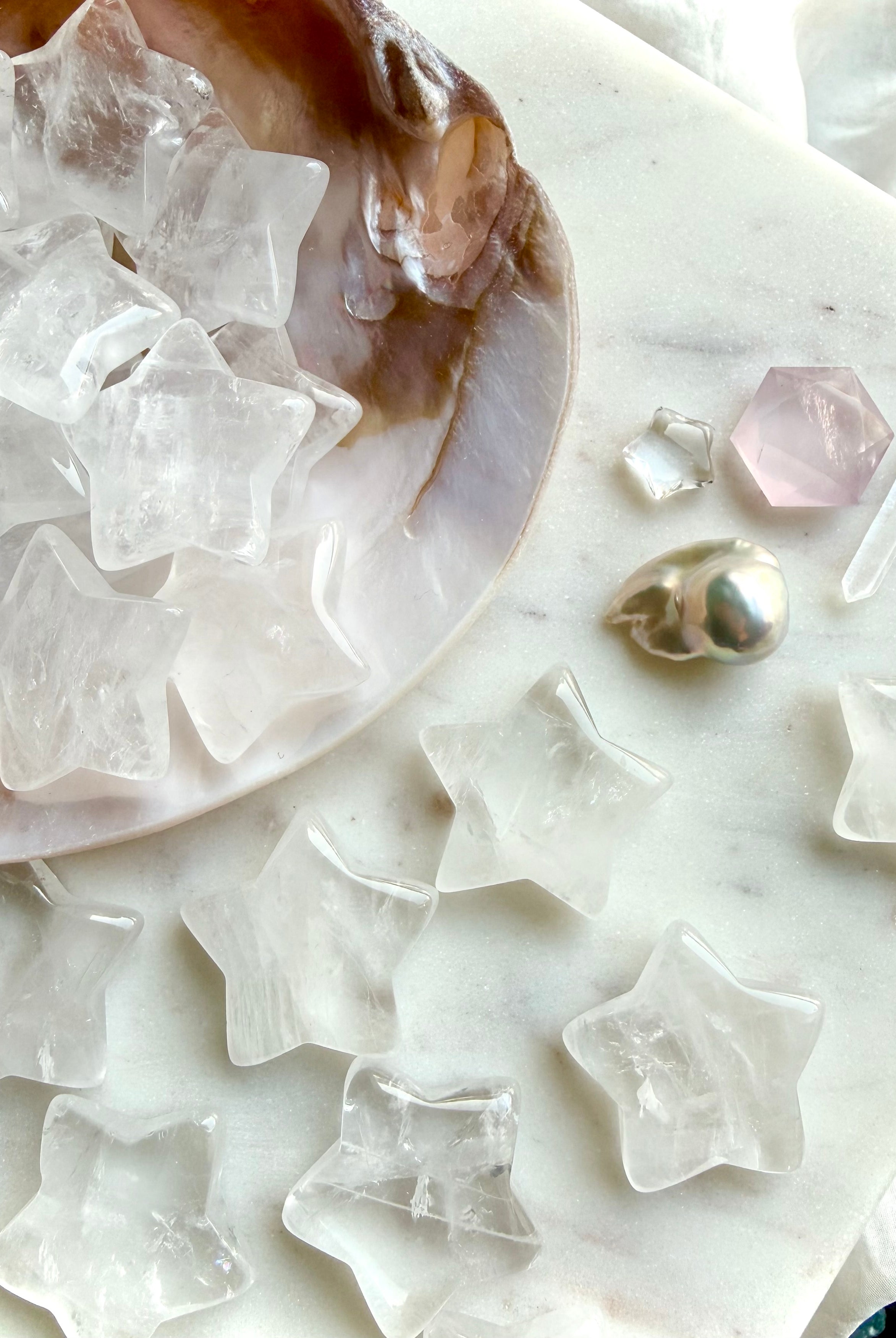 Closeup of Clear Quartz stars spilling out of a seashell onto granite surface with other celestial crystals, luminous chakra healing carvings