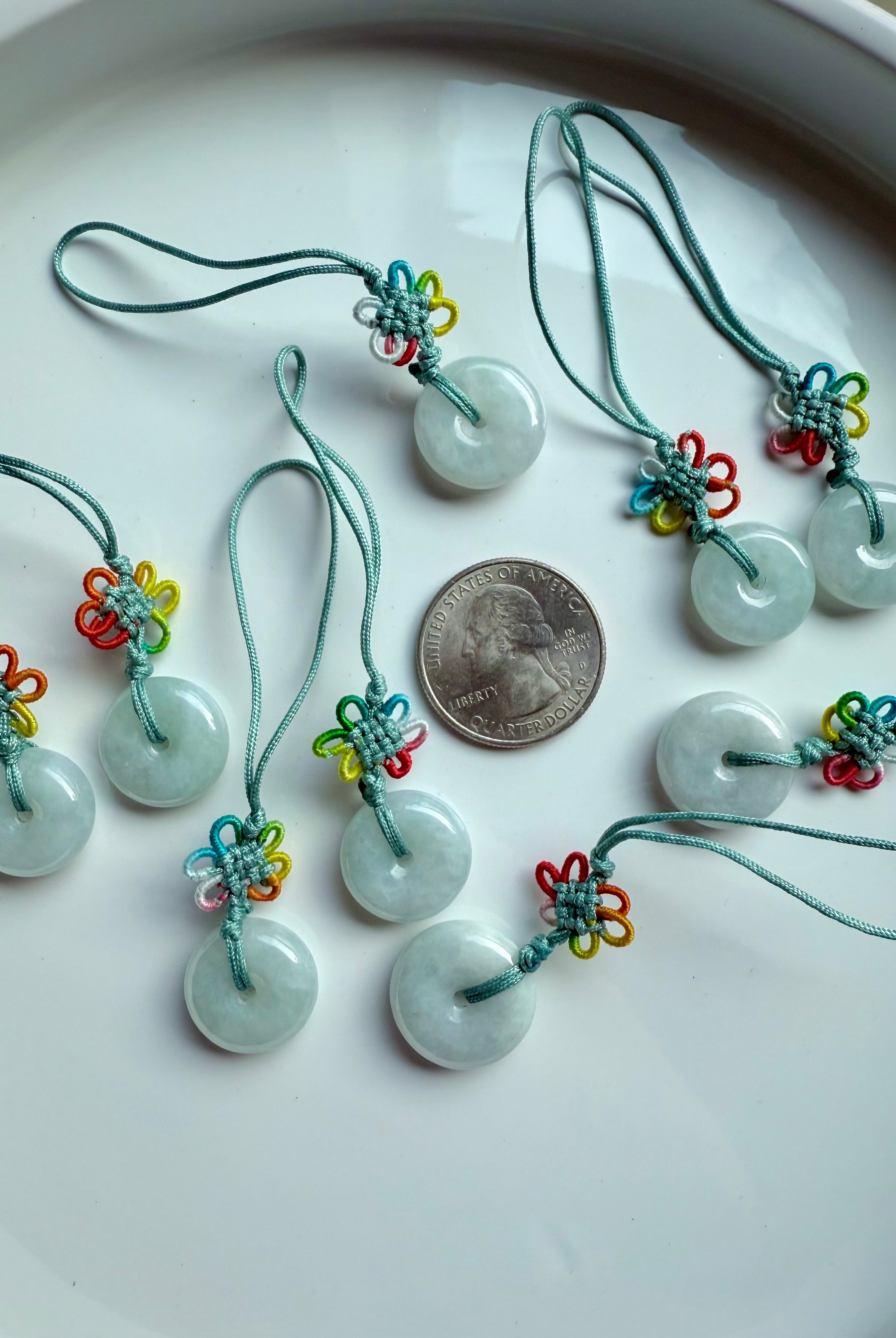 Jade donut charms with colorful knots arranged in a group beside a US quarter for size reference