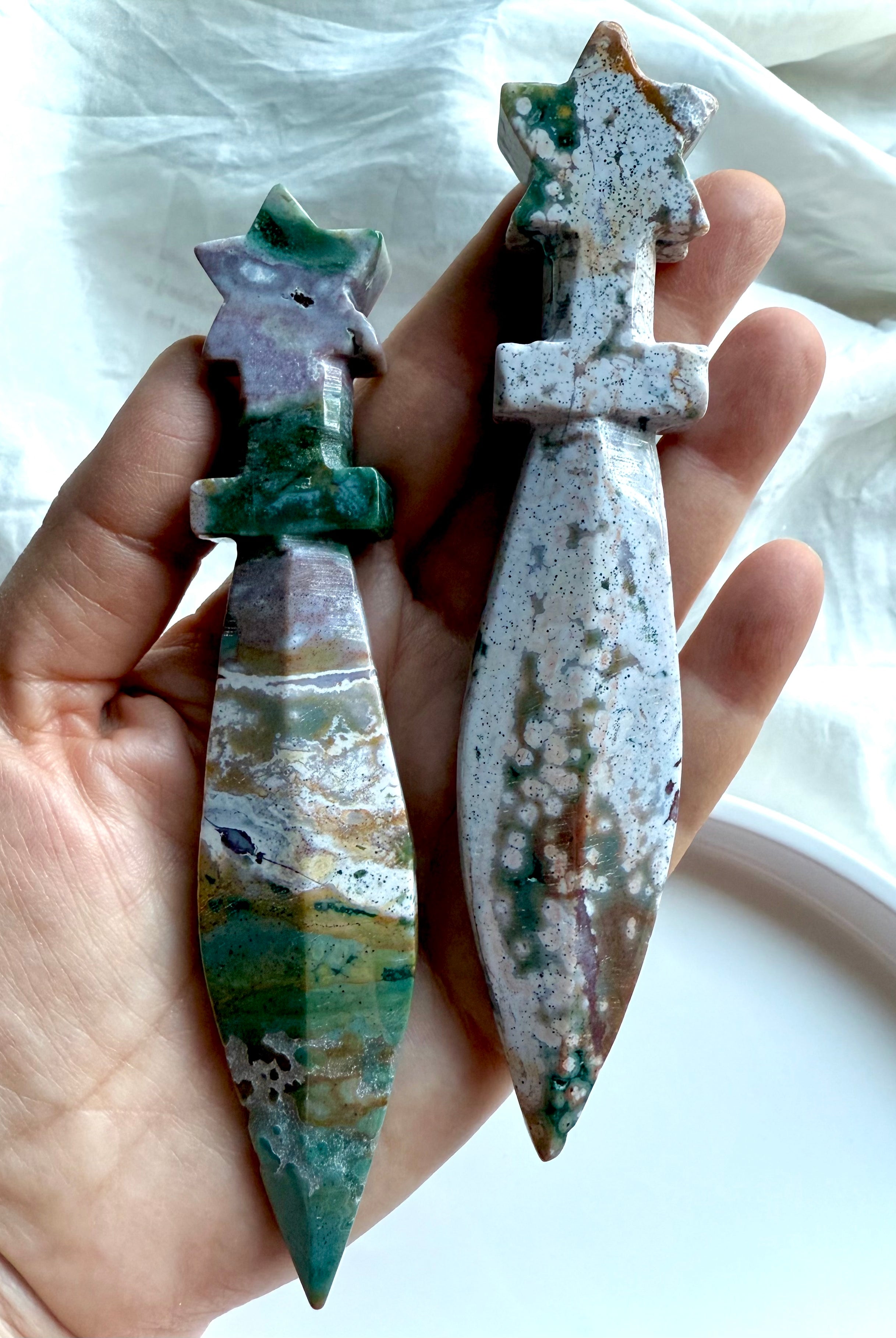 Two Ocean Jasper star knives with carved star handles and smooth stone blades, held in hand to show size and natural color variations