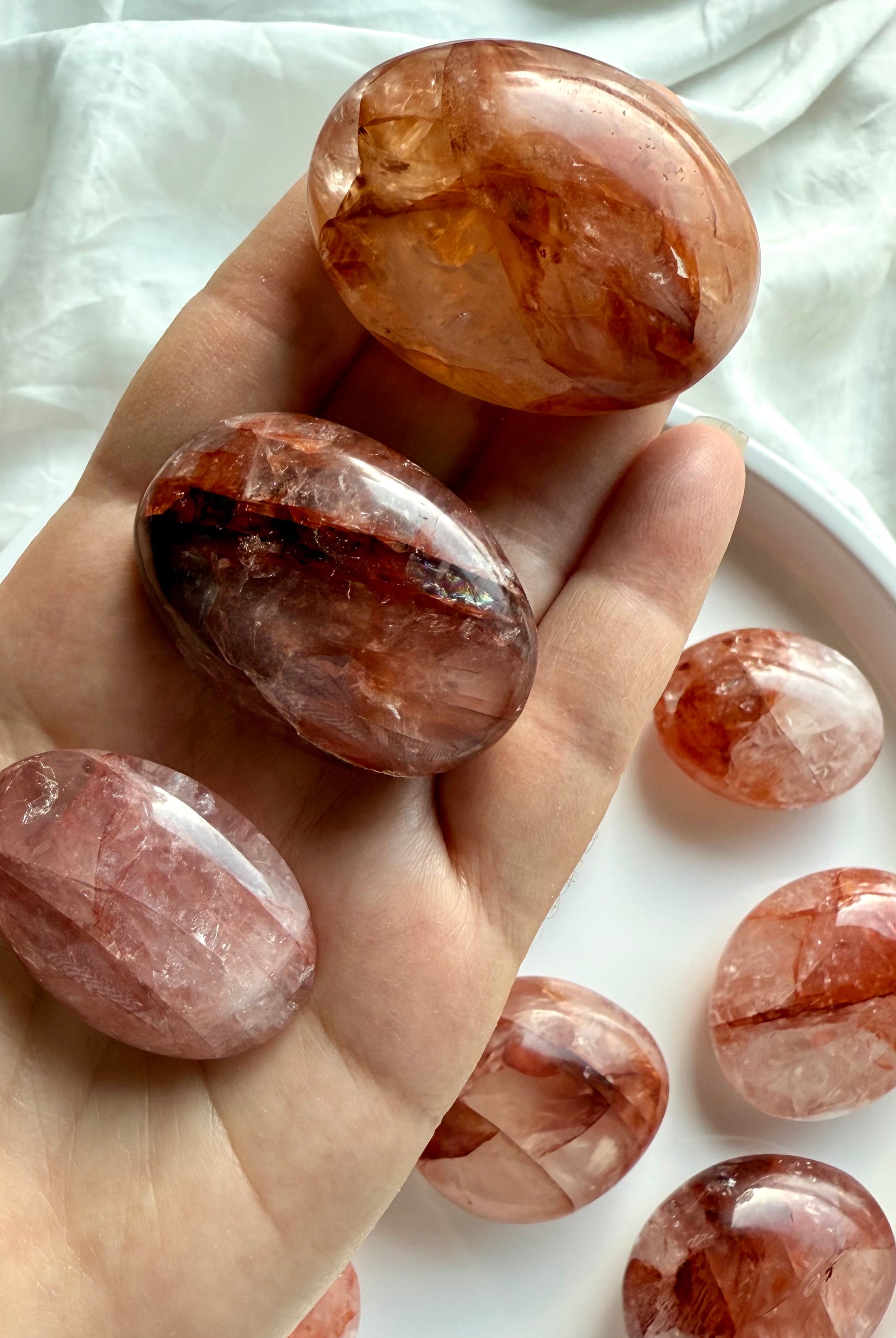 Hand holding polished Hematoid Quartz palm stones in red and orange hues for chakra balancing