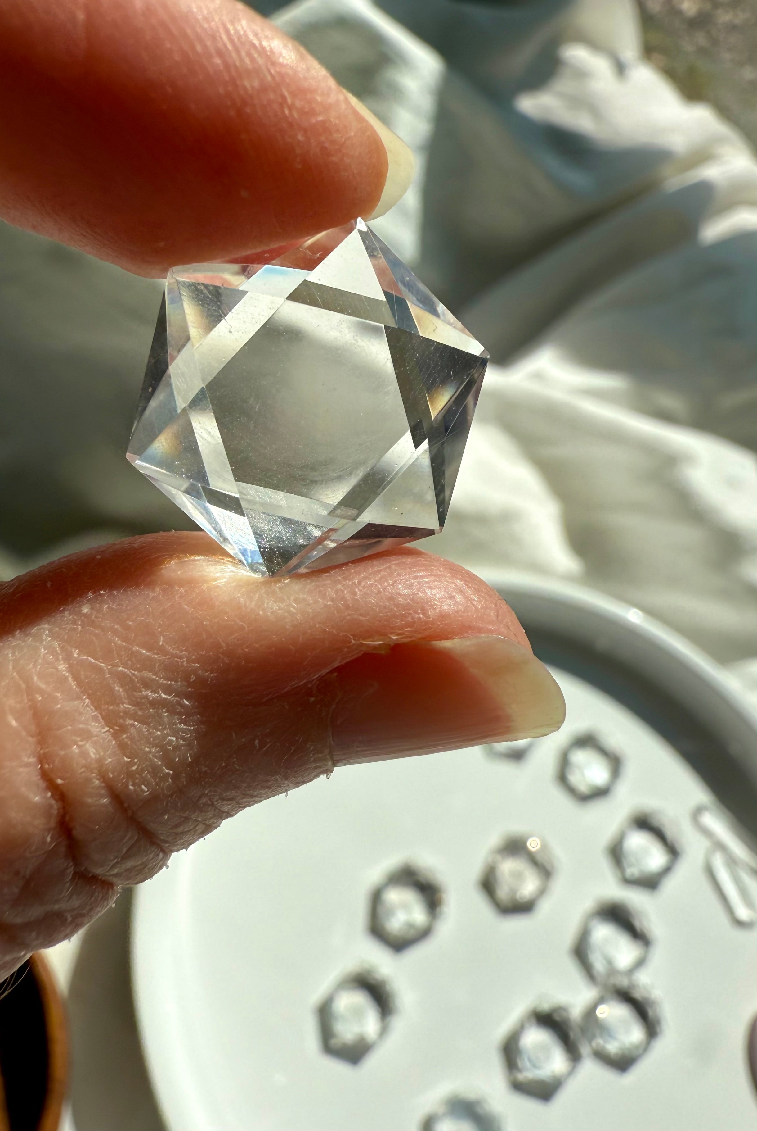 Closeup of Clear Quartz hexagon held to the light with plate of crystals blurred in background