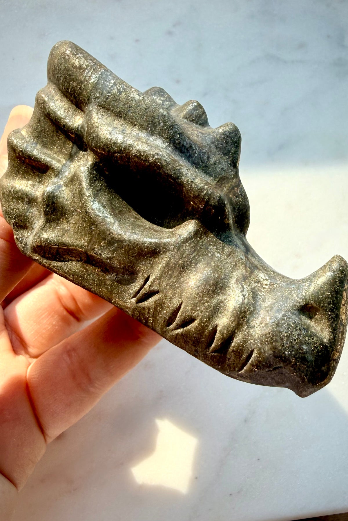Natural Pyrite dragon head carving with golden-bronze metallic luster, textured scales, and sculpted horns, held between fingers