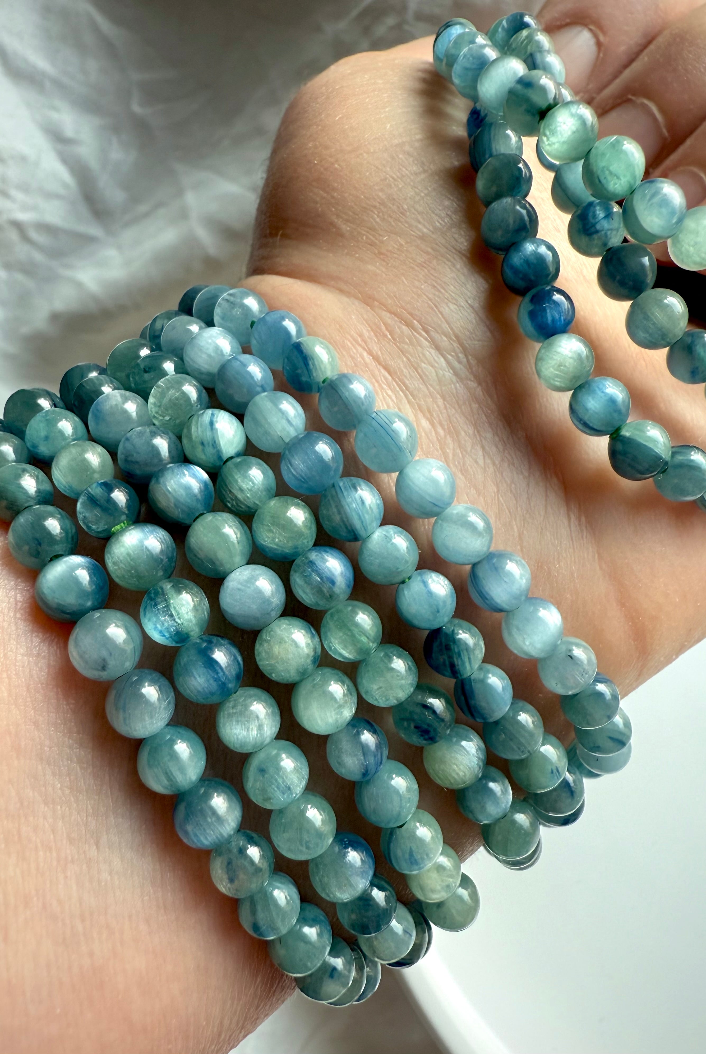 crystal bracelets stacked on arm in natural lighting showcasing the soothing aqua, seafoam, and indigo striations of kyanite beads
