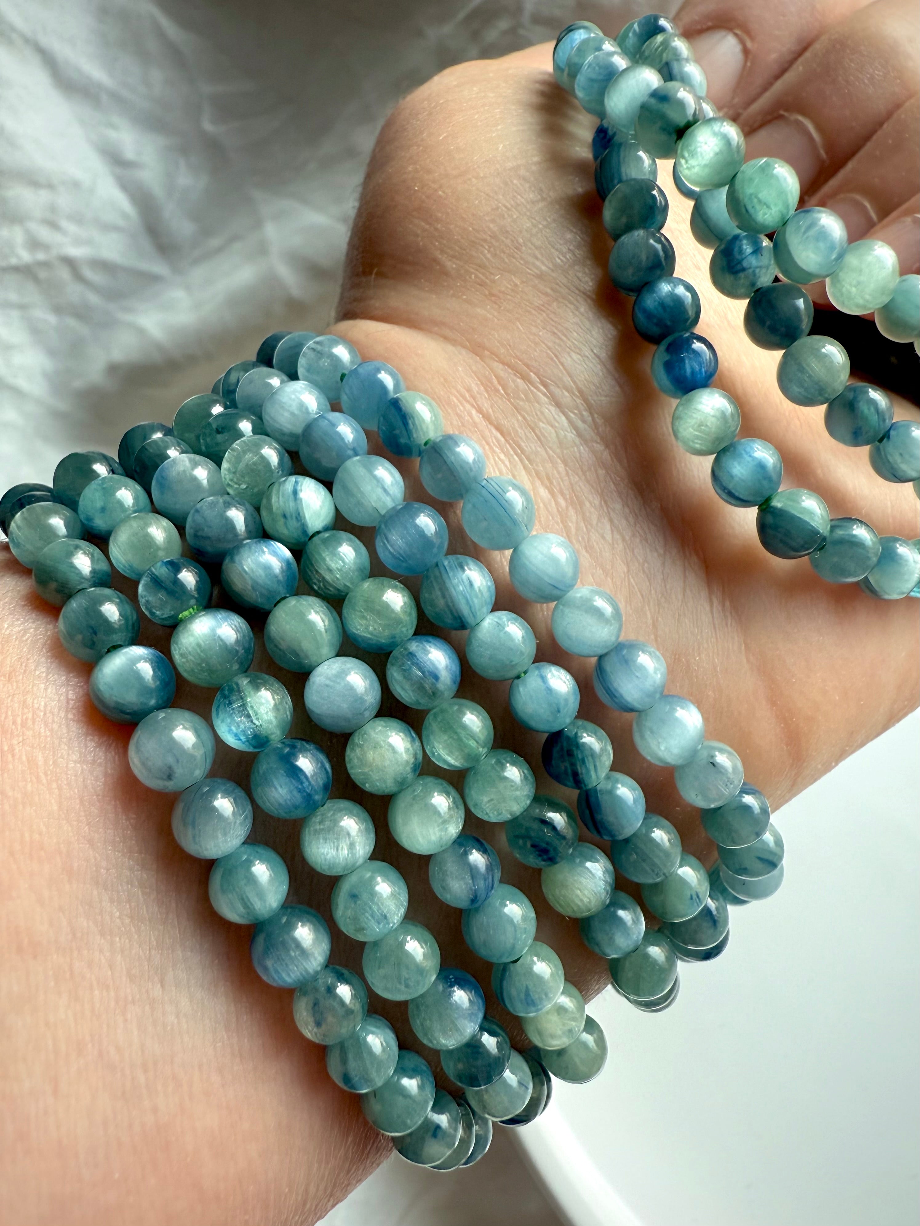 crystal bracelets stacked on arm in natural lighting showcasing the soothing aqua, seafoam, and indigo striations of kyanite beads