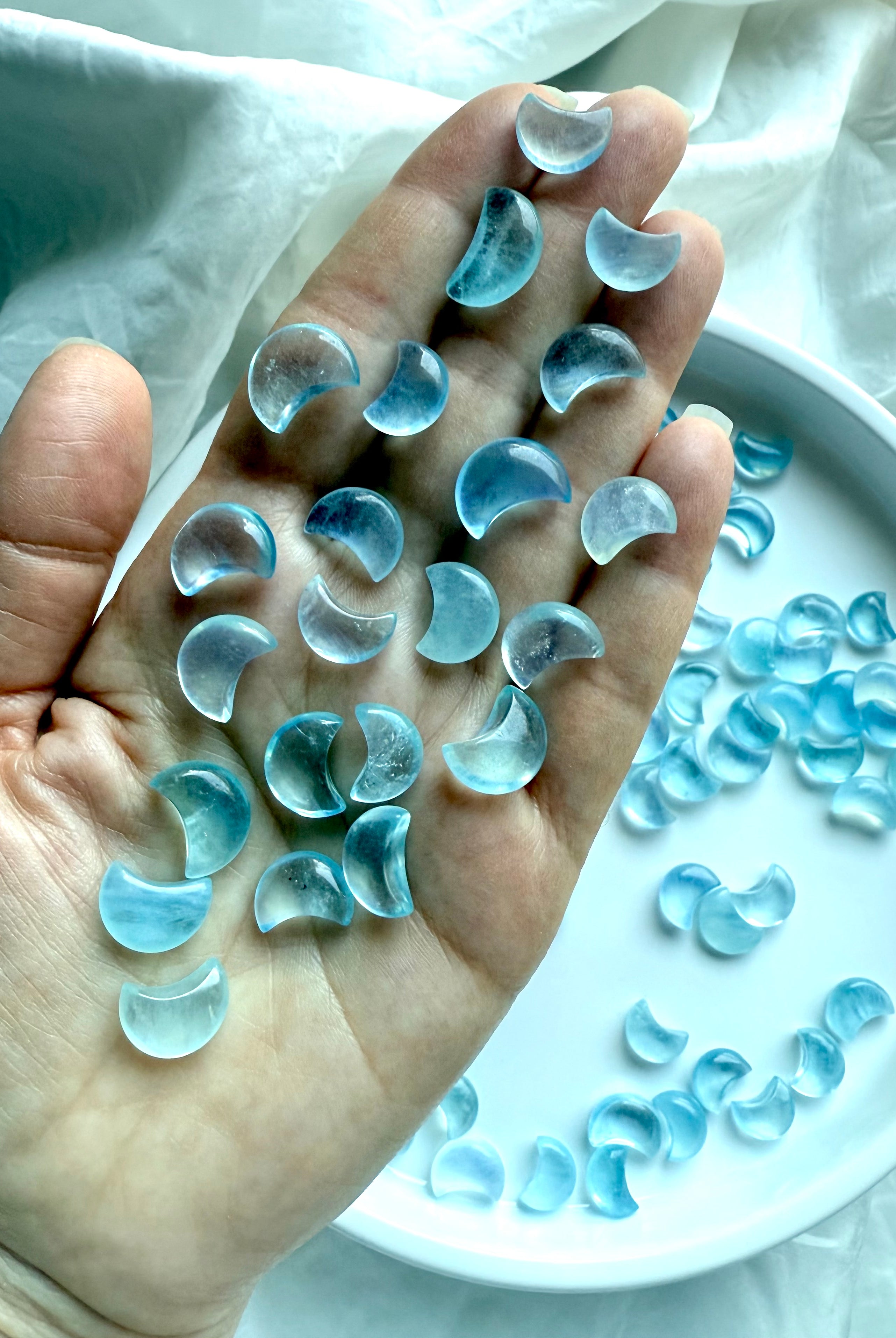 A hand holding a cascade of Aquamarine crescent moons, showing soft color variation, clarity, and polished shine