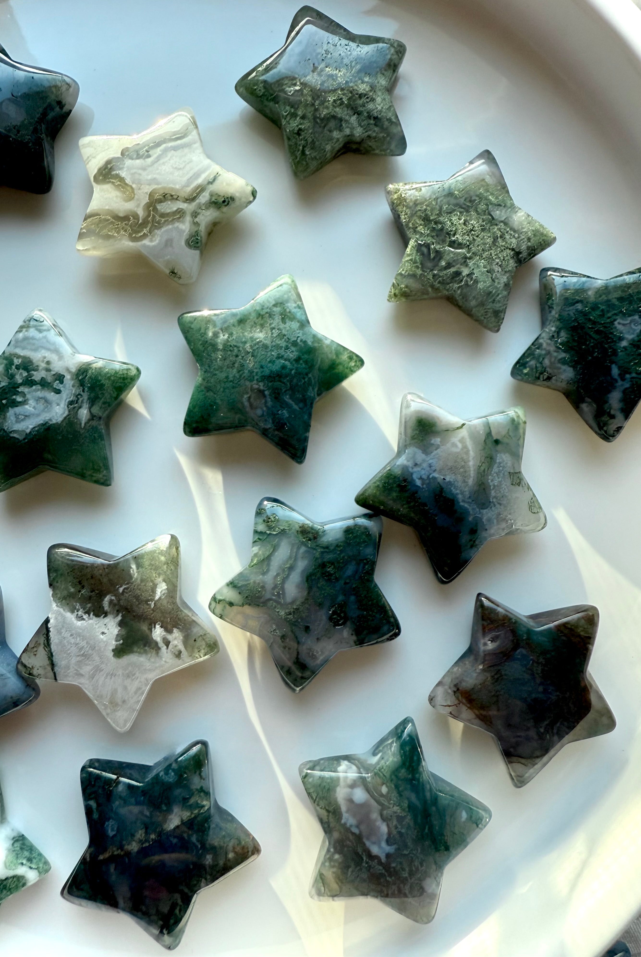 Assortment of polished Moss Agate stars on display tray, featuring deep forest green patterns and druzy-like inclusions — grounding crystal carving for heart chakra balance.