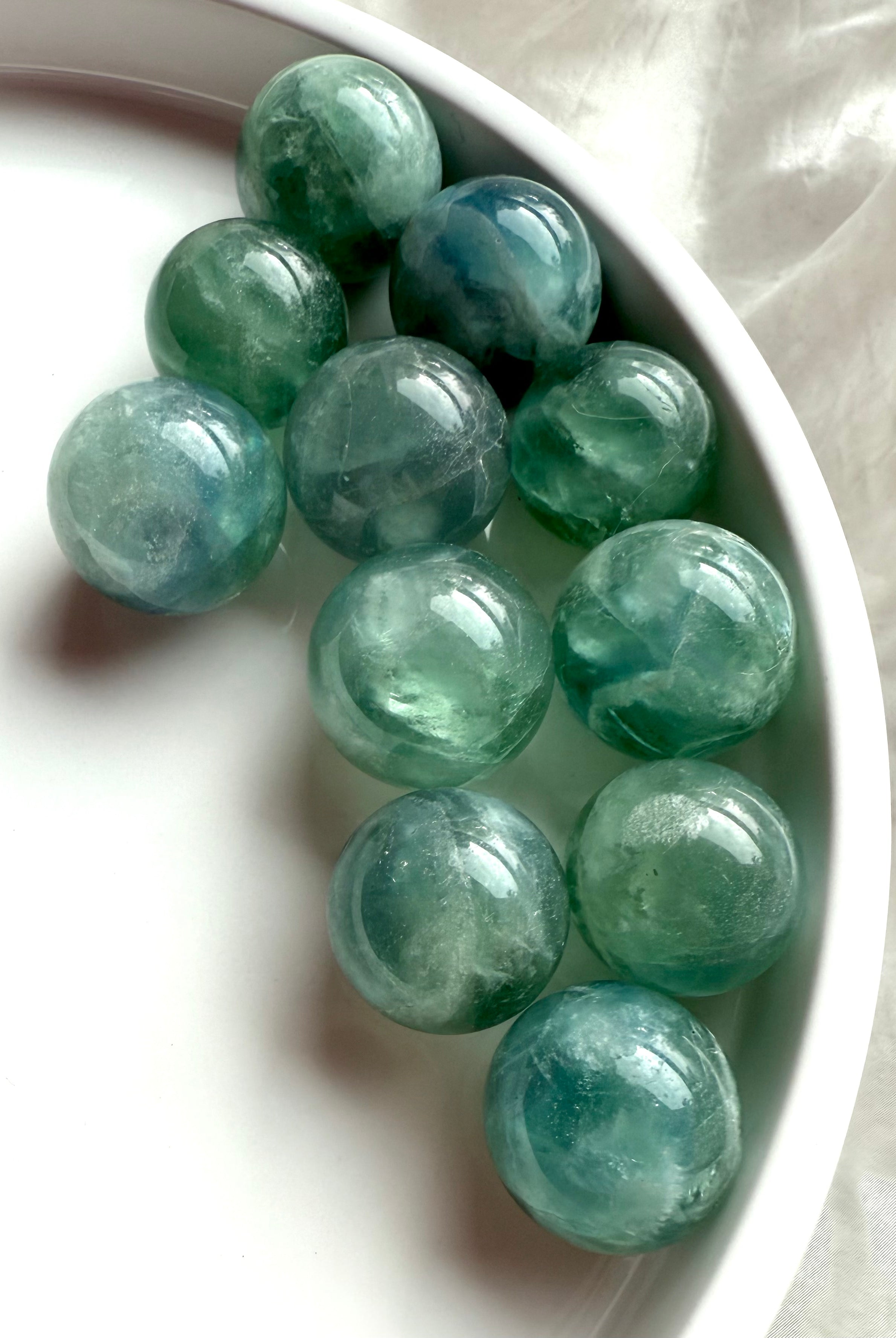 Mini teal Fluorite spheres with blue-green hues arranged on a white tray, healing crystals for clarity and Third Eye activation.